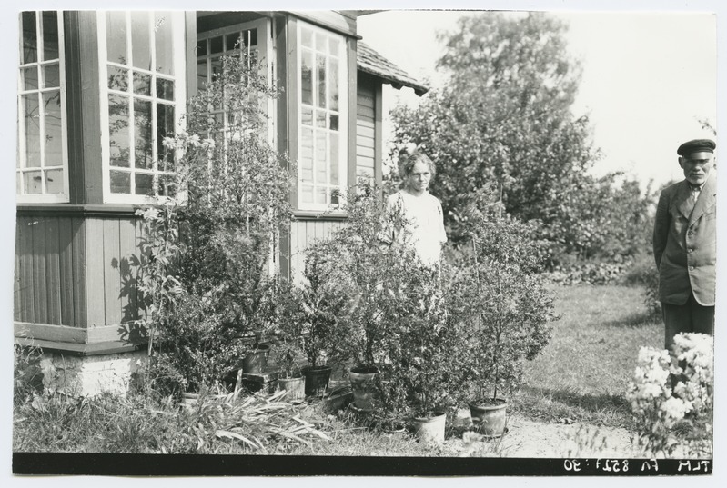 Verandaga maja välisvaade seisva mees- ja naisfiguuriga, 1920-ndatest aastatest.