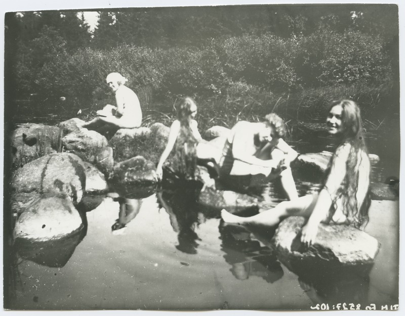 Grupifoto, neli naisfiguuri veekogu kaldal kividel istumas, umbes 1915. aastast.