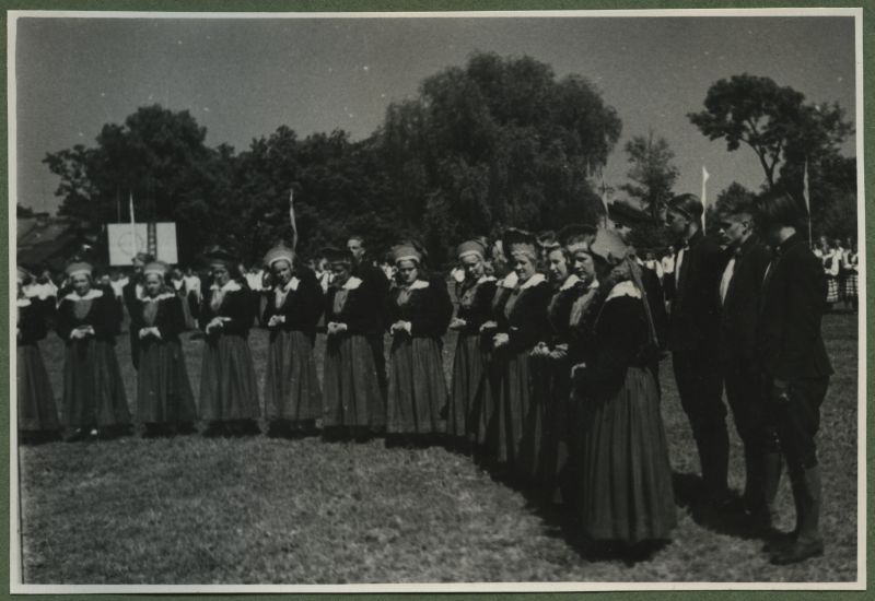 XII üldlaulupidu 28.-29. juunil 1947, Tallinnas.

Rahvariietes rahvatantsurühm seismas rahvakunstiõhtul 12. üldlaulupeo eelõhtul Kadrioru staadionil. Rahvatantsijad seisavad kaares kahes reas, eesreas seisavad naisrahvatantsijad, taga meesrahvatantsijad. 
Tagaplaanil paistavad teised rahvatantsijad.