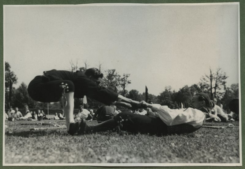 XII üldlaulupidu 28.-29. juunil 1947, Tallinnas.
Rahvariietes noormehed tantsimas/võimlemas rahvakunstiõhtul 12. üldlaulupeo eelõhtul Kadrioru staadionil. Esiplaanil kaks rahvariietes noormest, kellest üks on pikali ja teine kummargil, hoides üksteisel käest kinni. Taustal näha teisi rahvatantsijaid murul istumas.