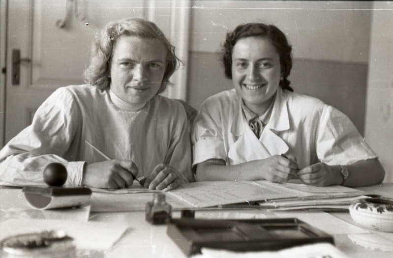 Kaks naist kitlites kirjutuslaua taga istumas