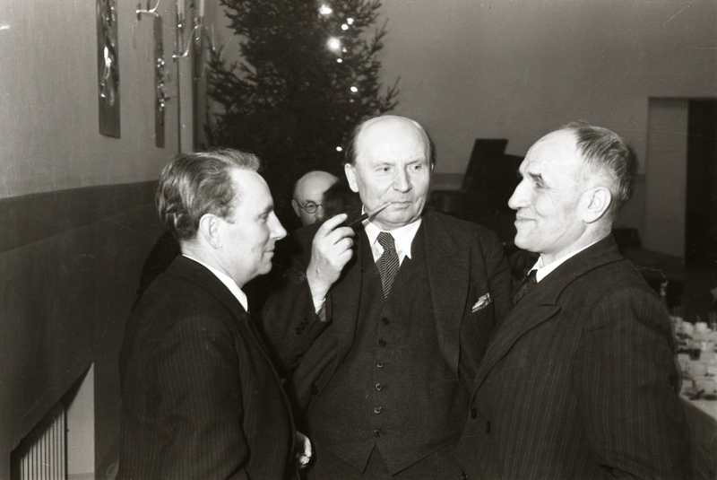 Kunstnik Jaan Vahtre (keskel) ja kaks meest seismas, taamal jõulupuu (Noor-Eesti kirjastuse jõulupidu 18. detsembril 1938)