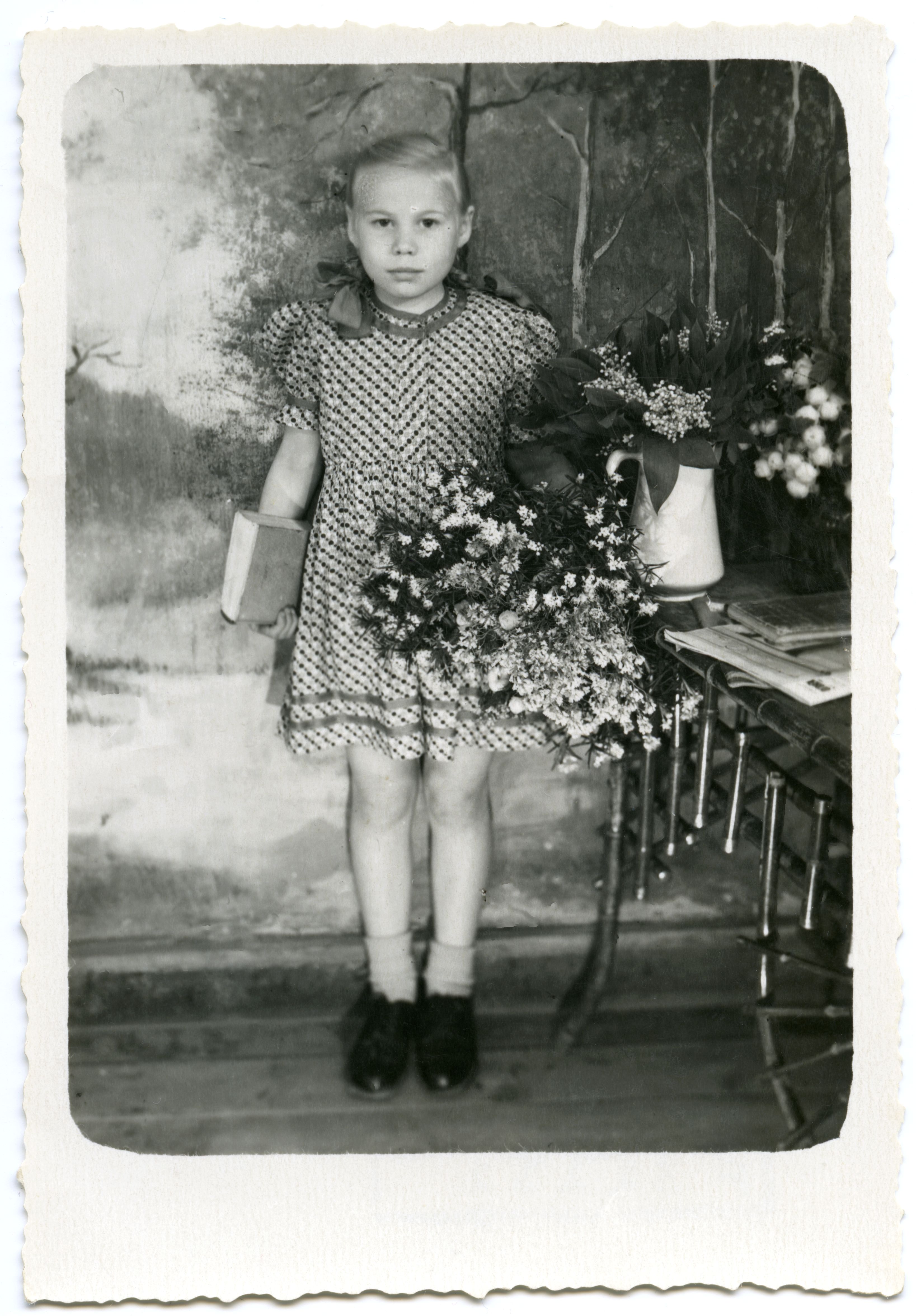 Tütarlaps (umbes 7.aastane) kirjus suvekleidis lillede ja raamatuga maalitud fooni taustal.