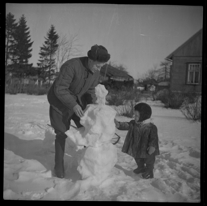 Väike poiss isaga lumememme tegemas