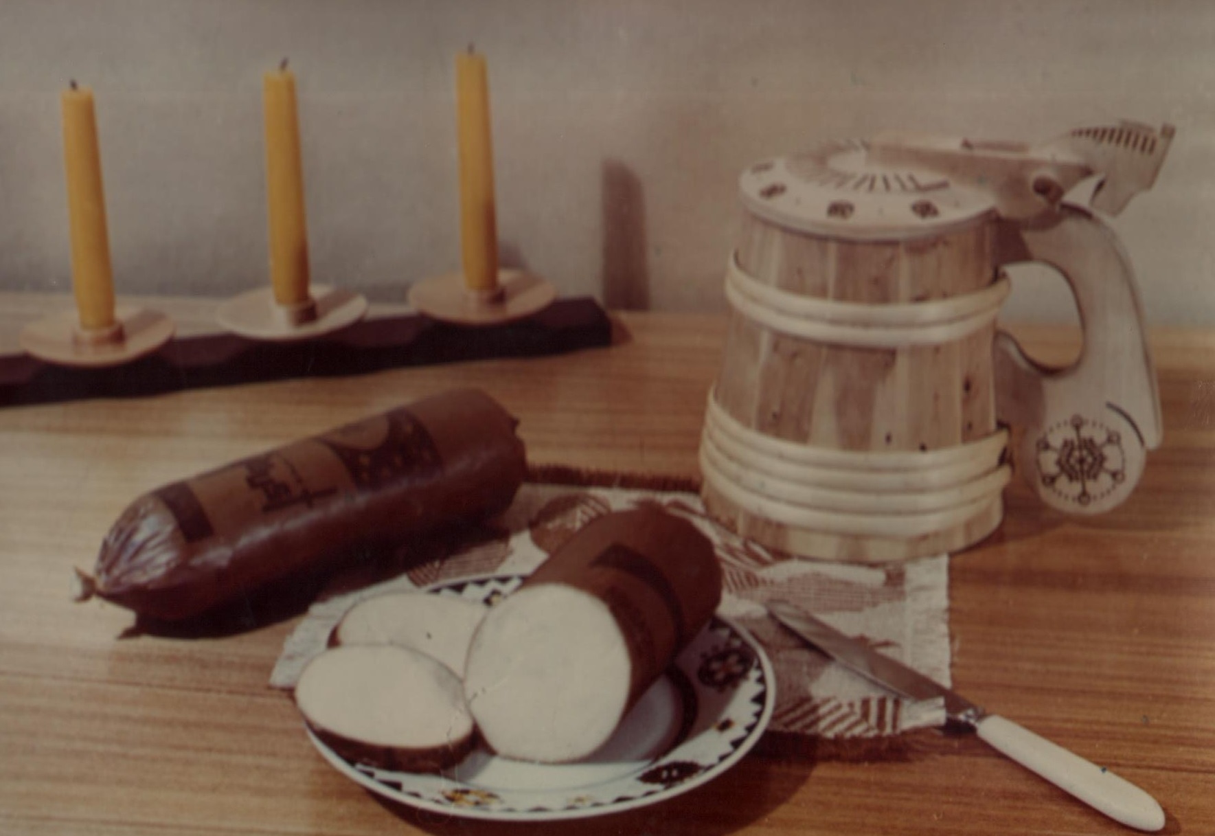 Lauakujund: sulatatud vorstjuust taldrikul, laual suveniir õllekapp; tagaplaanil küünlad