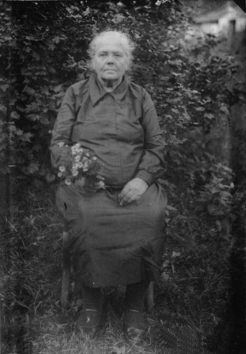 Klaasnegatiiv. Vana naine istub õues toolil, käes lilled