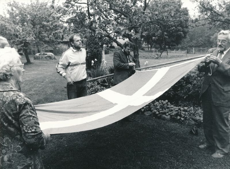 Foto. Rootsi Kuningriigi peakonsuli Leningradis hr. Bengt Akerreni Vormsil 21.juunil 1988.a.
Fotol vasakult Vormsi abimetsaülem Ants Varblane, Eestirootslaste Kultuuriseltsi esimees Ain Sarv ja seltsi aseesimees Maido Limbak konsuli poolt kingitud Rootsi lipuga. 
Foto: Arvo Tarmula.