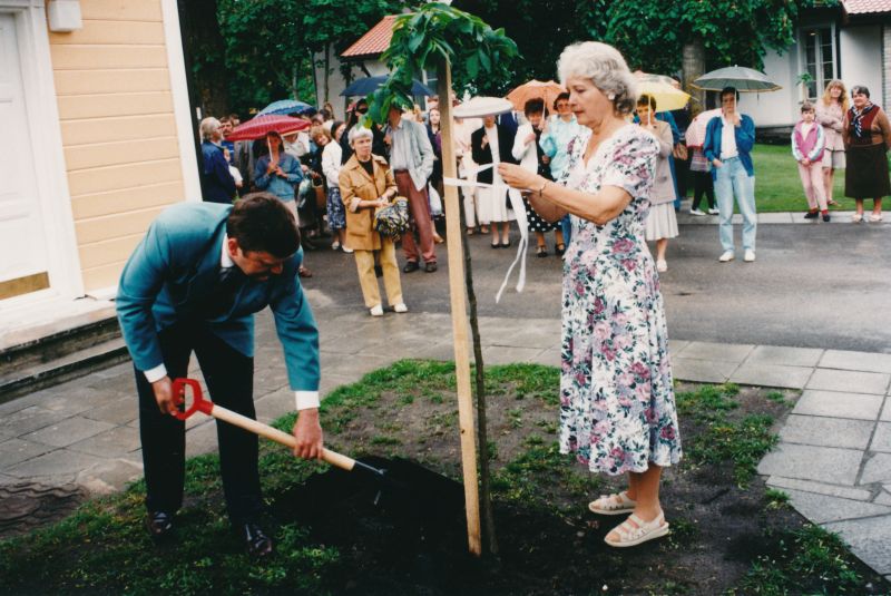 Foto. Ernst Enno 120.sünniaastapäeva tähistamine Haapsalus, Lahe 8 õuel 8.juunil 1995.a.  Puud istutavad Ernst Enno tütretütar Elin Toona ja Lääne maavanem Hannes Danilov.
Värvifoto.