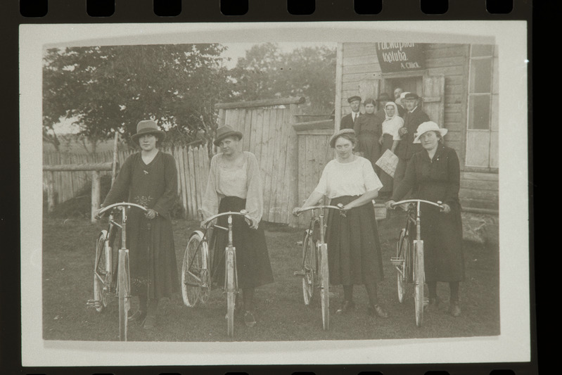 Glücki töökoda tagaplaanil, ees neli naist jalgratastega