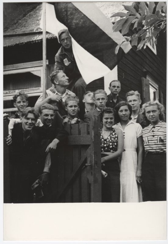 Noormehed ja tütarlapsed maja hoovis koos Eesti lipuga.