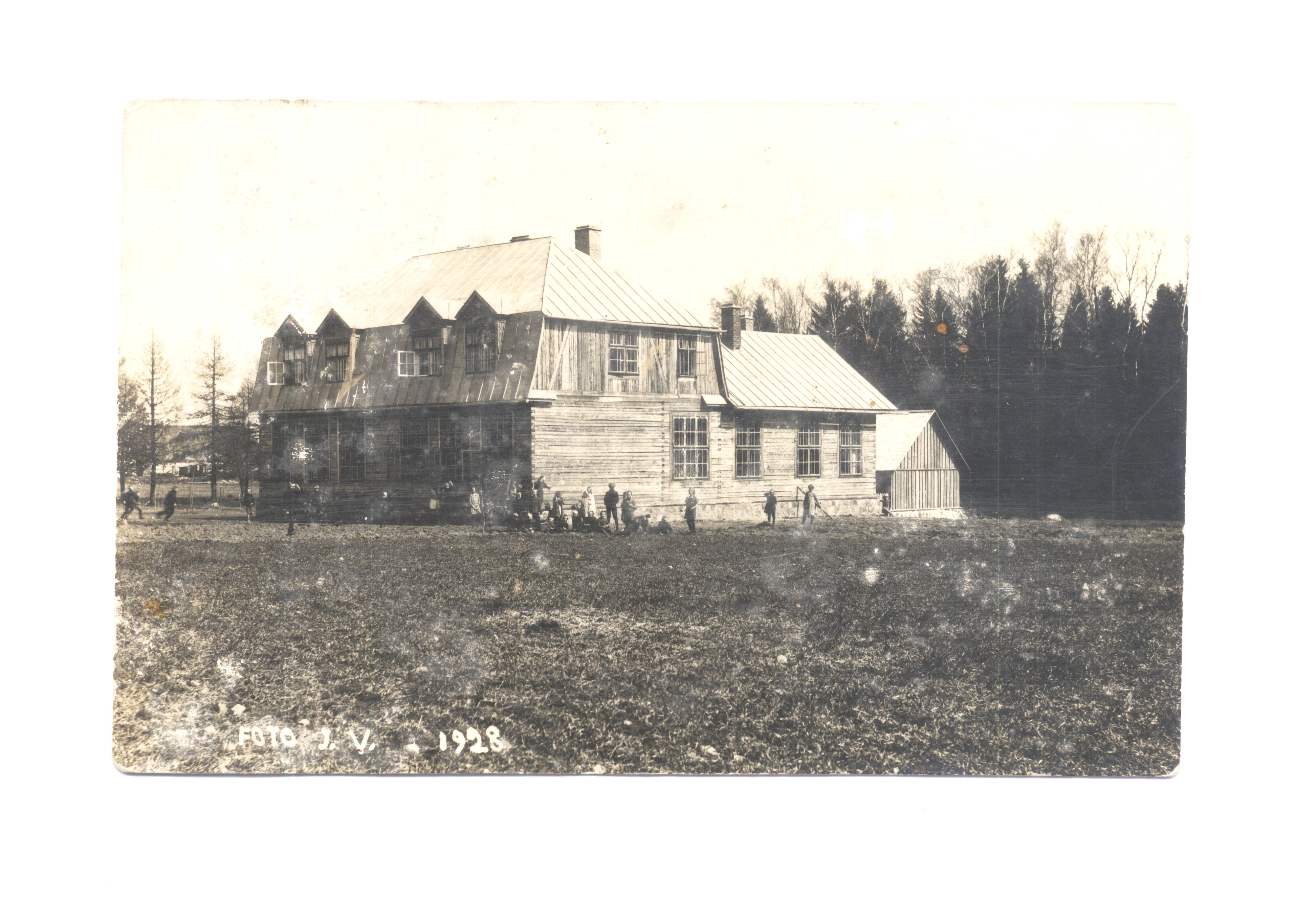Must-valge foto vaatega puust koolihoonele, mille ees mängivad koolilapsed