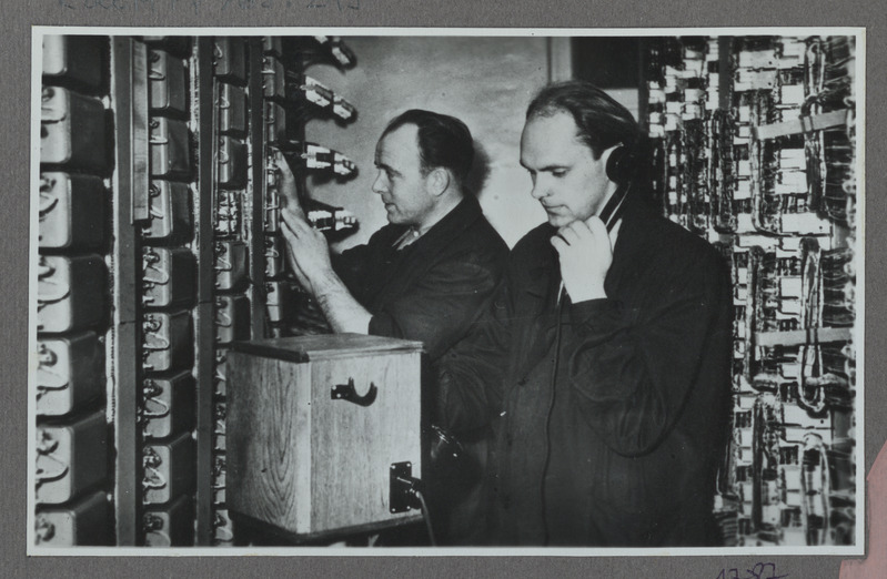 Eesti raudtee: elektromehaanikud Kask (vasakul) ja Kroon Tallinna uues raudtee automaattelefonijaamas seadmeid kontrollimas, 1958, foto: Oskar Sildam