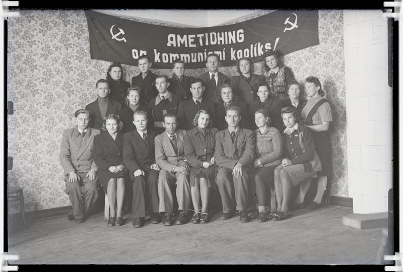 Ametiühingu tegelaste grupipilt loosungi( Ametiühing on kommunismi kooliks!) taustal.