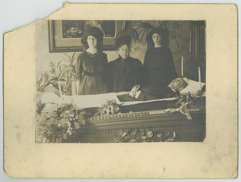 Kolm naist leinariietes avatud kirstu ääres.