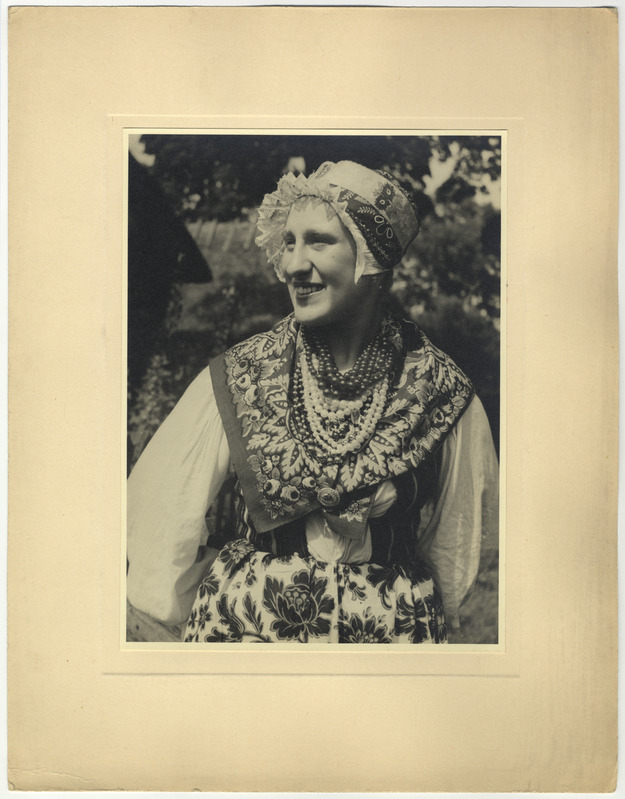 Rahvariietes naine tanuga, tagaplaanil taluhooned.