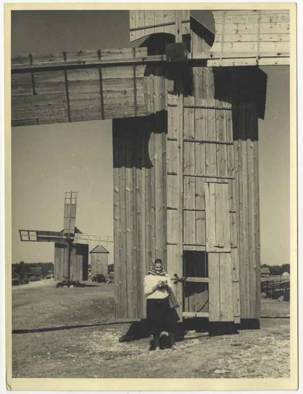 Vormsi rahvariietes naine kott käes seismas pukktuuliku tiibade juures.