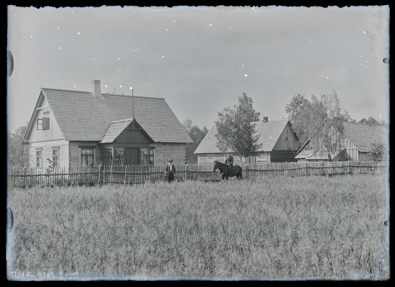 Vaade: tundmatu talu, keskel seisab aia ääres mees, temast paremal ratsanik hobusel.