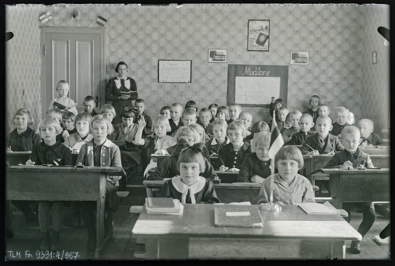 Vaade klassiruumi. Tuhala kool Oru mõisas. Tundmatud õpilased ja õpetaja. Tagumises reas seisab püsti ja loeb raamatust Vilmar Kruus.