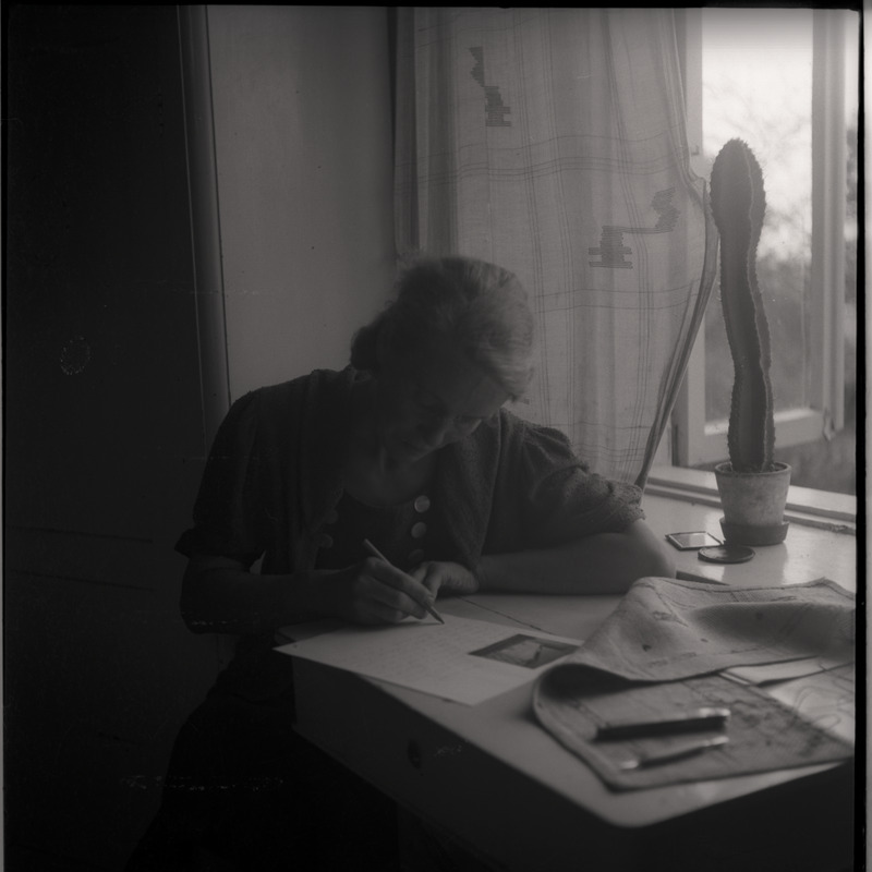 Magda Millistfer laua taga kirja kirjutamas, kõrval aknalaual kaktus