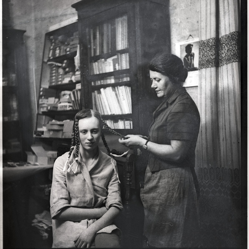 Ethel Malle Sarap ja Johanna Triefeldt toas patse punumas, taustal riiulid karpide ja raamatutega