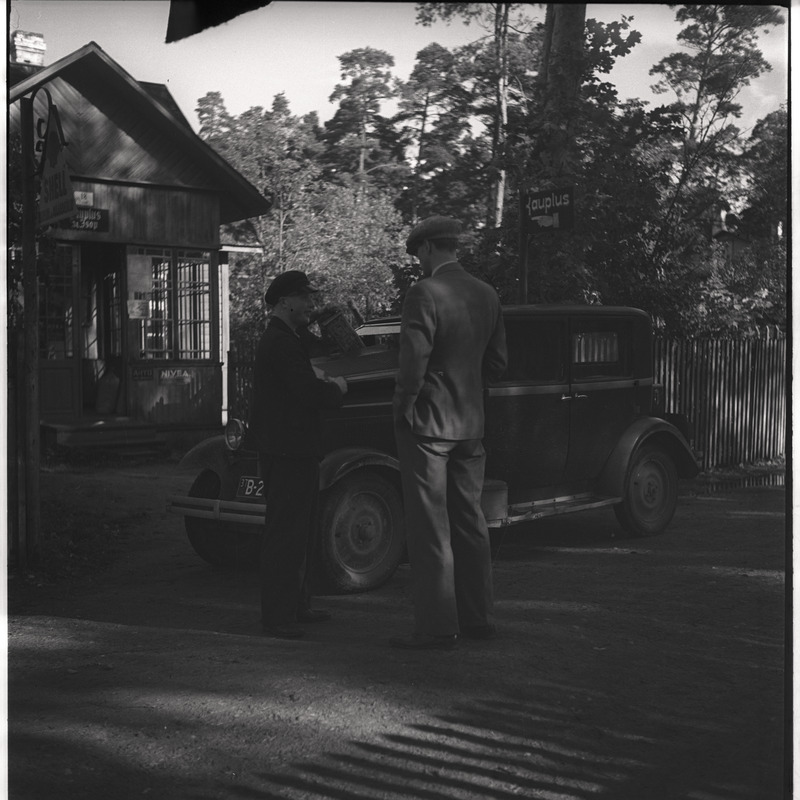Autojuht ja Otto Liiv seismas auto kõrval, kaupluse ees