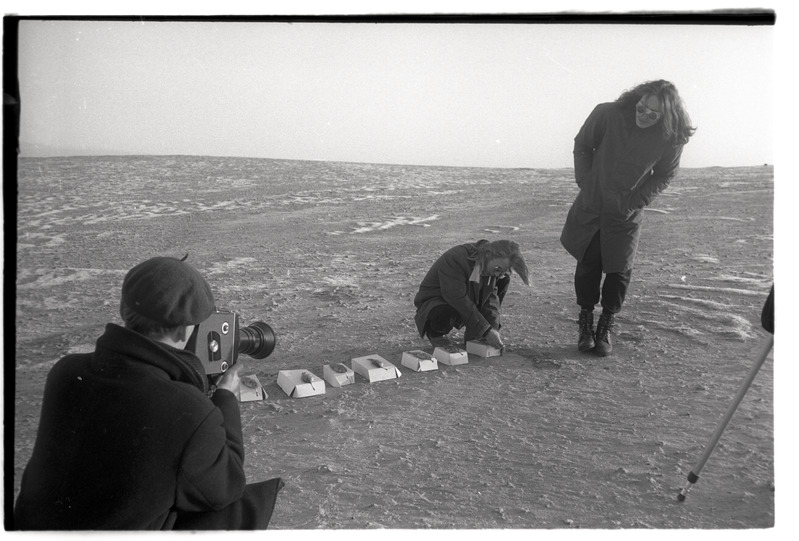 „Reportaaž 3. „Performance filmimine (tuleviku meenutuseks)““ - mehed jäädvustamas performance-etendust liivaväljal, kalad seatud ritta, sigaretid suus