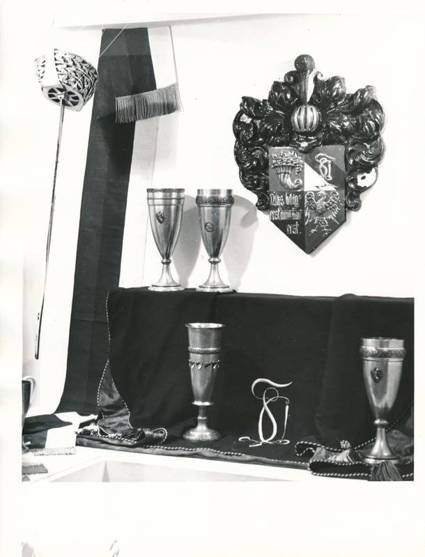 Üliõpilasorganisatsioonide näitus Tartu Linnamuuseumis 1989a. Vitriinis hõbepeekrid, suur puust vapp, õlalint.