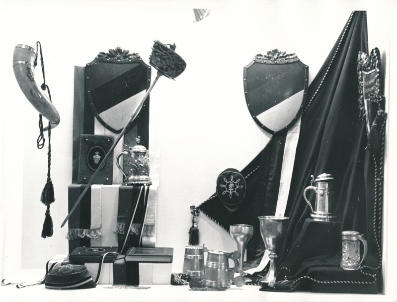 Üliõpilasorganisatsioonide näitus Tartu Linnamuuseumis 1989a. Hõbekannud, -peekrid, puust vapid, teklid, õlalindid, raamatud, rapiir.