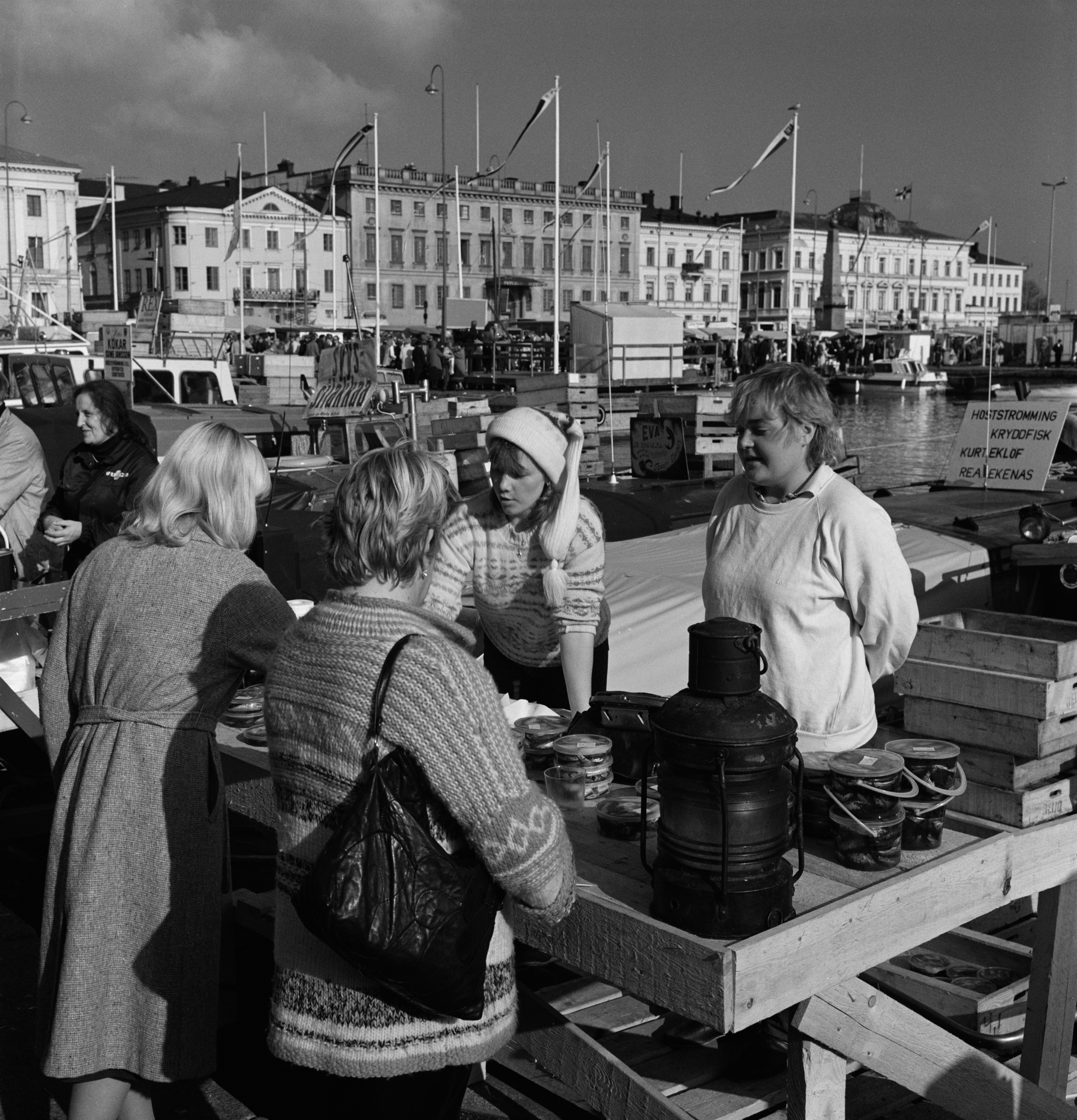Silakkamarkkinat Eteläsatamassa. Maustettua silakkaa myydään kalastajaveneestä Kolera-altaan reunalla. Taustalla Pohjoisesplanadui 1-9.