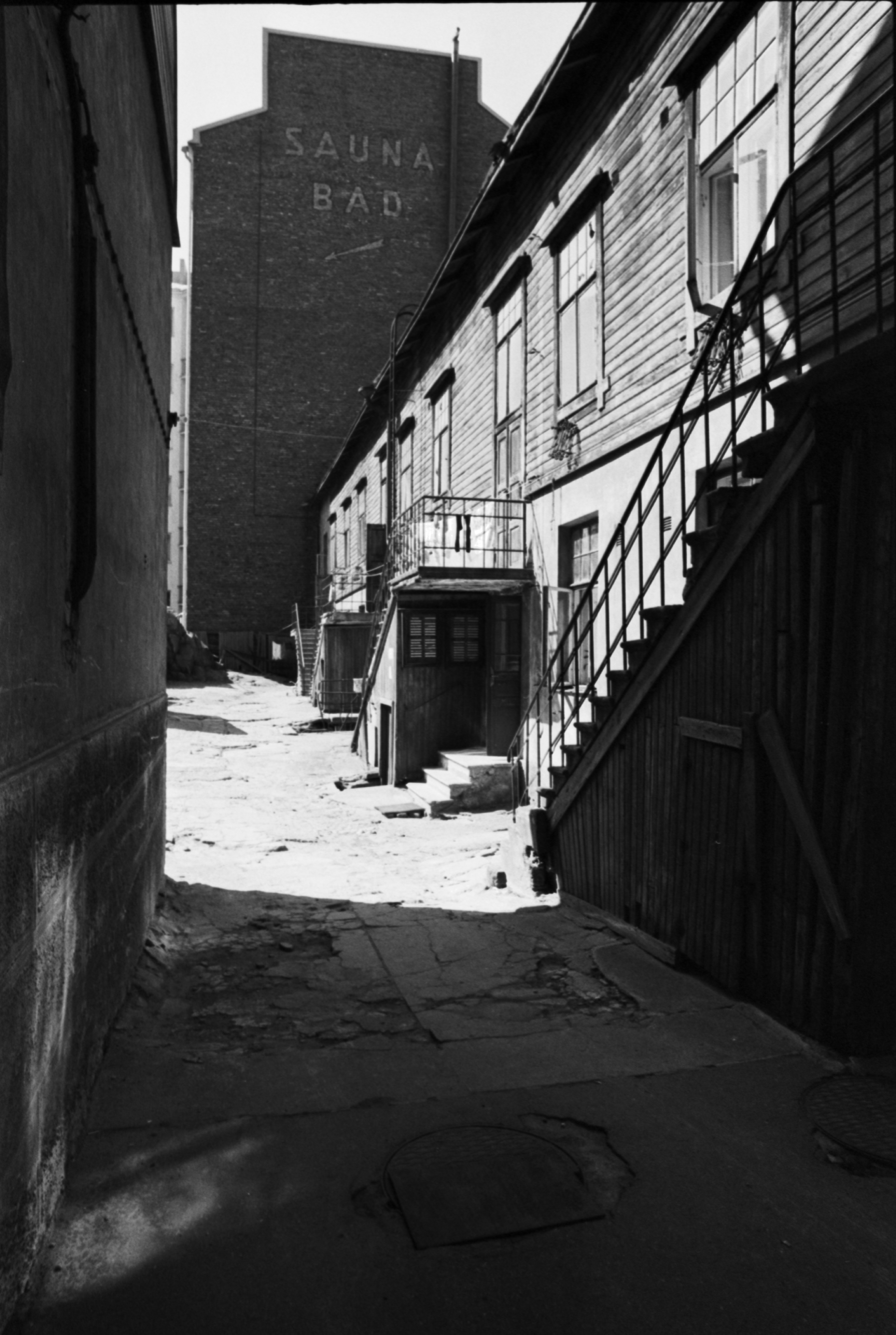 Fleminginkatu 16. Näkymä Fleminginkatu 16:n pihalle. Oikealla kaksikerroksinen puutalo, taustalla kerrostalo, jonka päädyssä teksti SAUNA BAD.