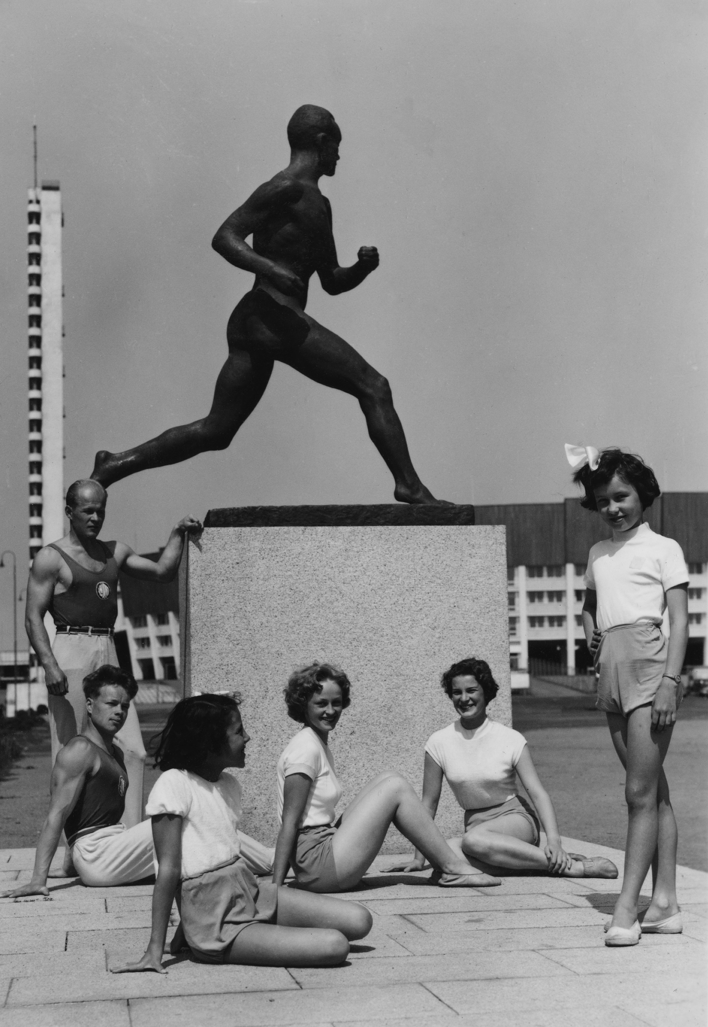 Urheilijoita Paavo Nurmen patsaan edessä olympialaisten aikaan Stadionin etukentällä. Taustalla Olympiastadion ja stadionin torni.
