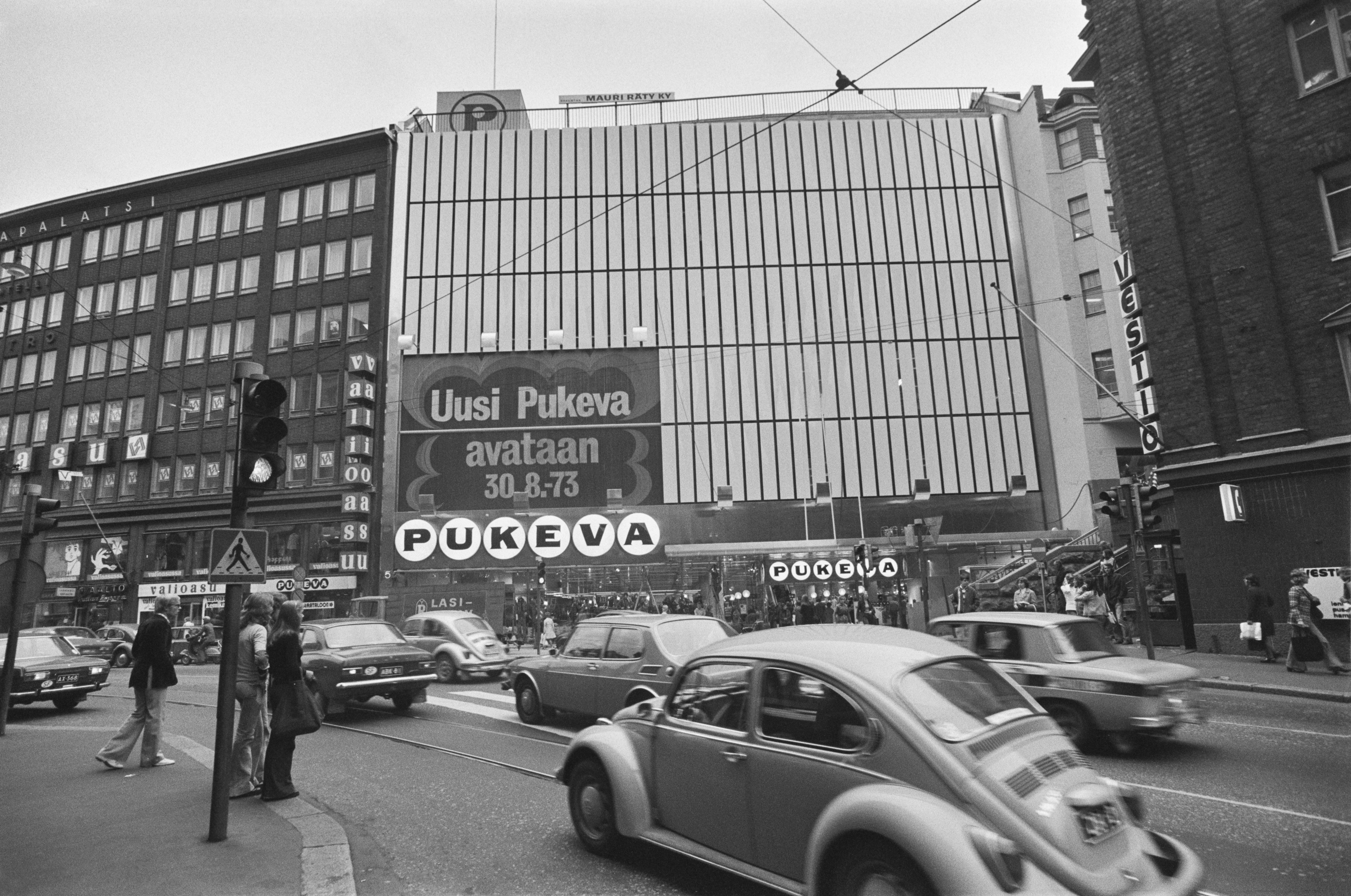 Kaisaniemenkatu 5. Pukevan uudistuneen tavaratalon julkisivua Kaisaniemenkadun suunnalta laajennusosan valmistuttua. Seinässä teksti: Uusi Pukeva avataan 30.8.1973.