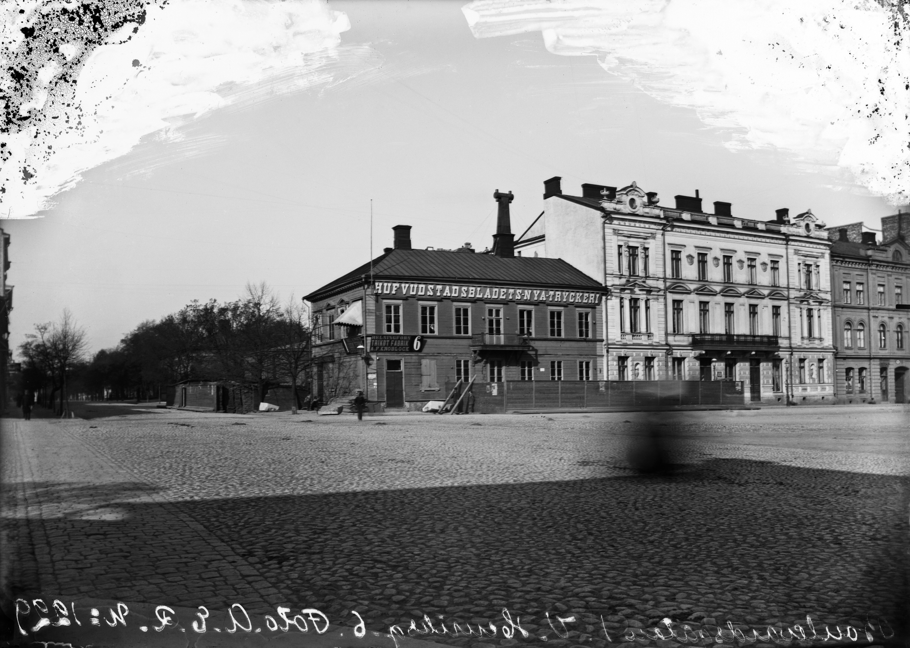 Läntinen Heikinkatu 6, 8 (=Mannerheimintie 2, Bulevardi 1), puurakennuksessa Hufvudstadsbladetin uuden kirjapainon ("Hufvudstadsbladets Nya Tryckeri") ja Helsingin Kudin Tehtaan myymälän ("Helsingfors Trikot Fabrik, A. F. Knoblock") mainoskyltit. Taustalla Bulevardin alussa Jenny Florinin talon pihamaa. Kulmassa olevan puurakennuksen paikalle on vuonna 1890 rakennettu Theodor Höijerin uusrenessanssityylinen kerrostalo, ja kuvassa talon edessä oleva aita liittyy ilmeisesti puurakennuksen purkutyömaahan.