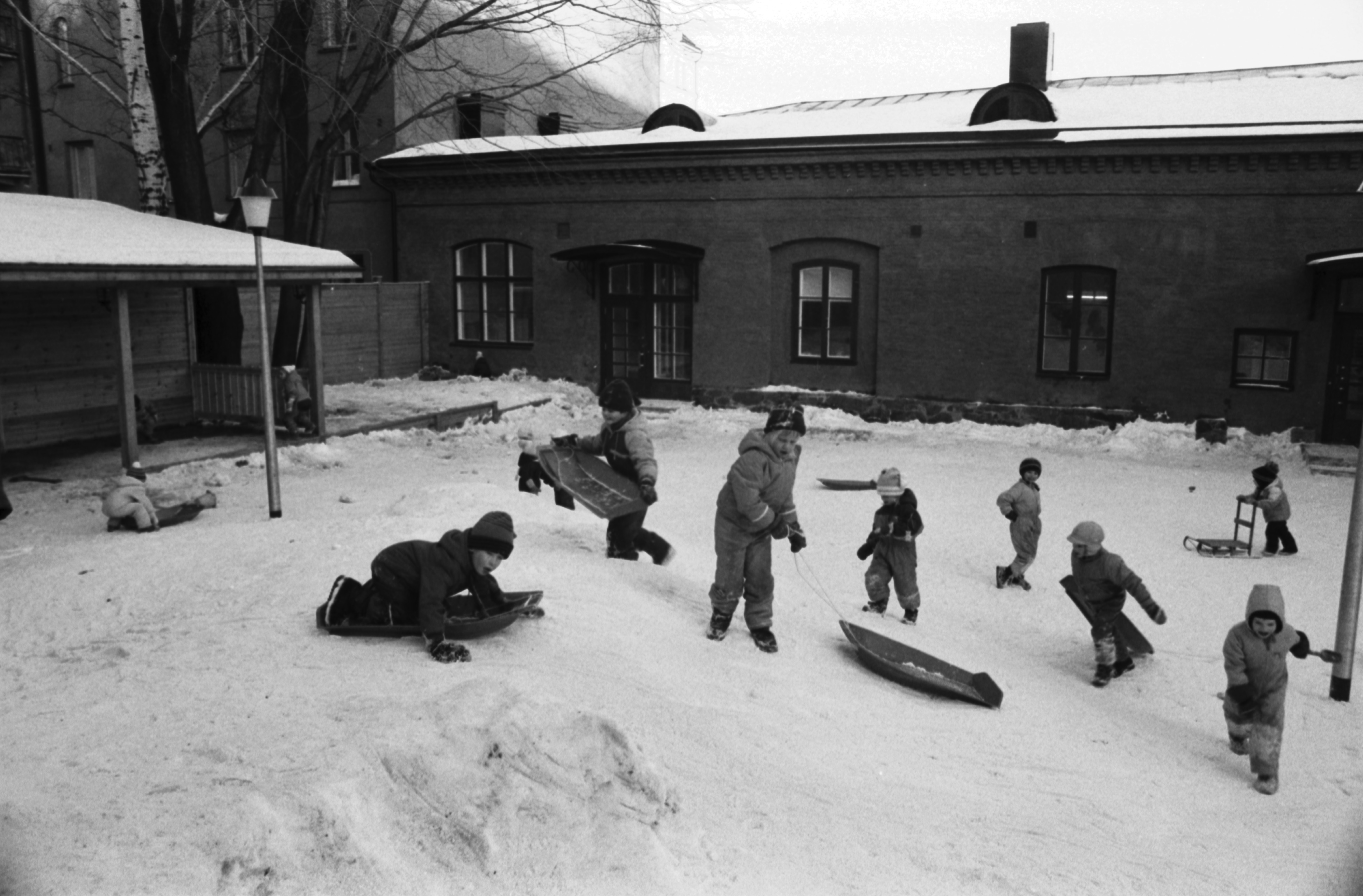 Aleksanterinkatu 1. Lapsia laskemassa pulkalla päiväkoti Aleksin lumisella pihalla.