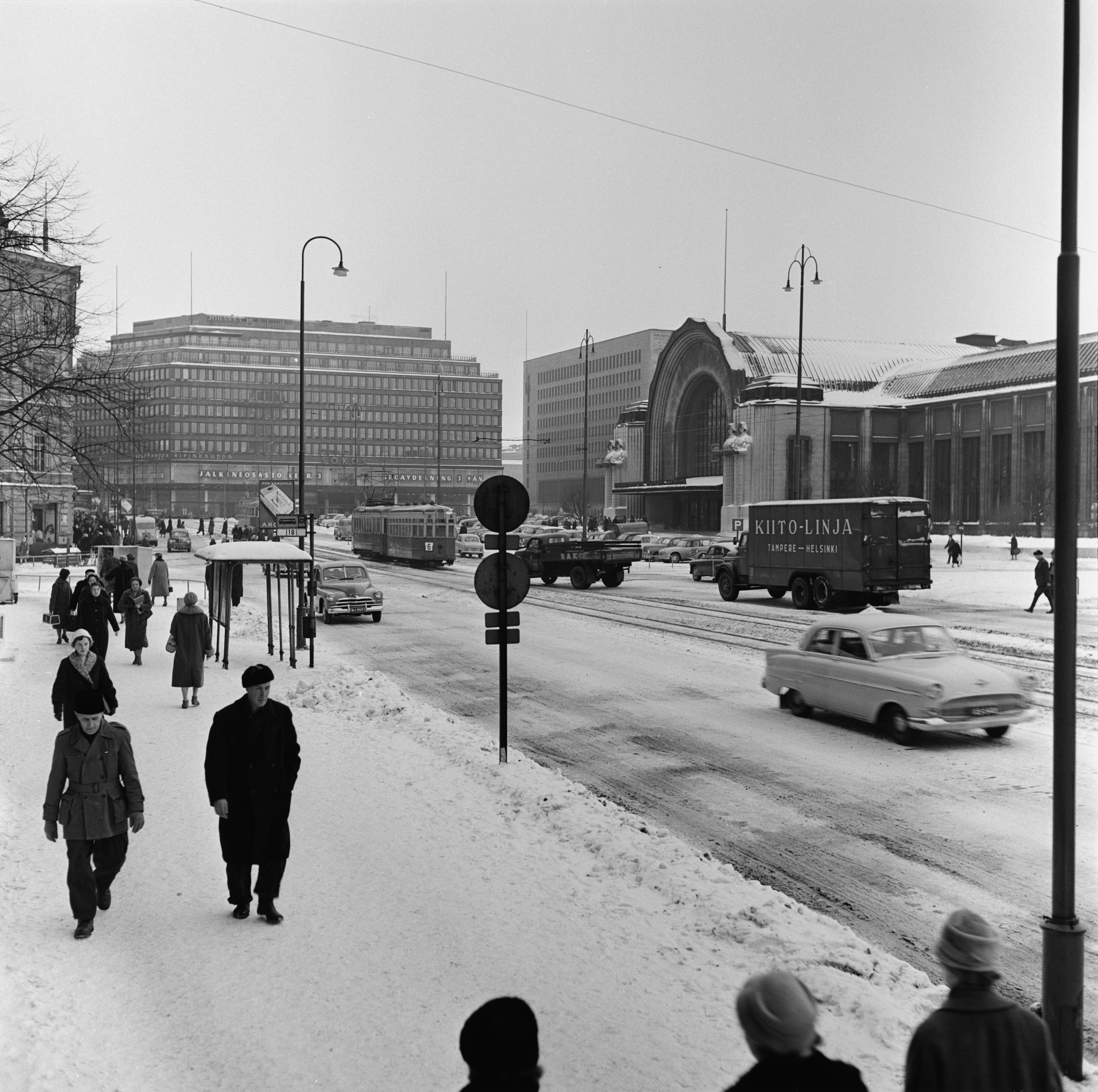 Jalankulkijoita ja liikennettä Kaivokadulla Ateuneumin edustalla. Taustalla Sokoksen tavaratalo, Postitalo ja Rautatieasema.