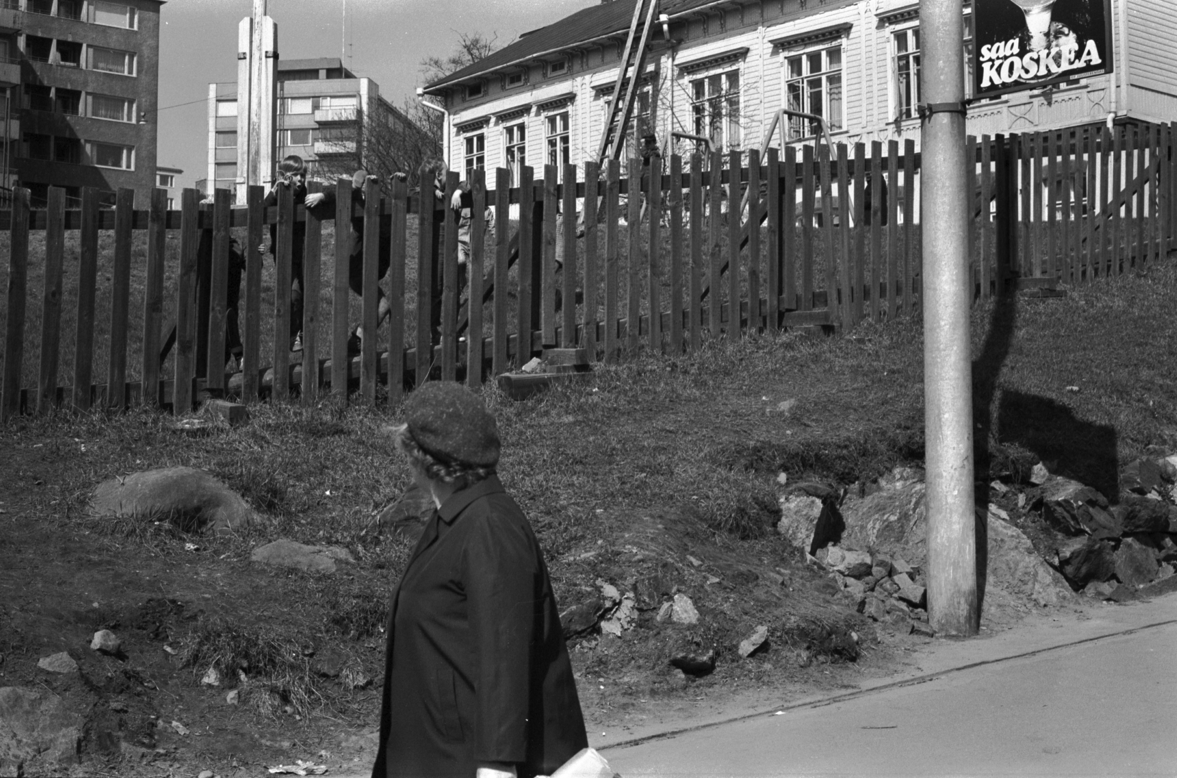 Porthaninkatu 2. Lapsia kurkkimassa säleaidan takana Tukholman päiväkodin pihalla Porthaninkadun ja Siltasaarenkadun kulmassa.