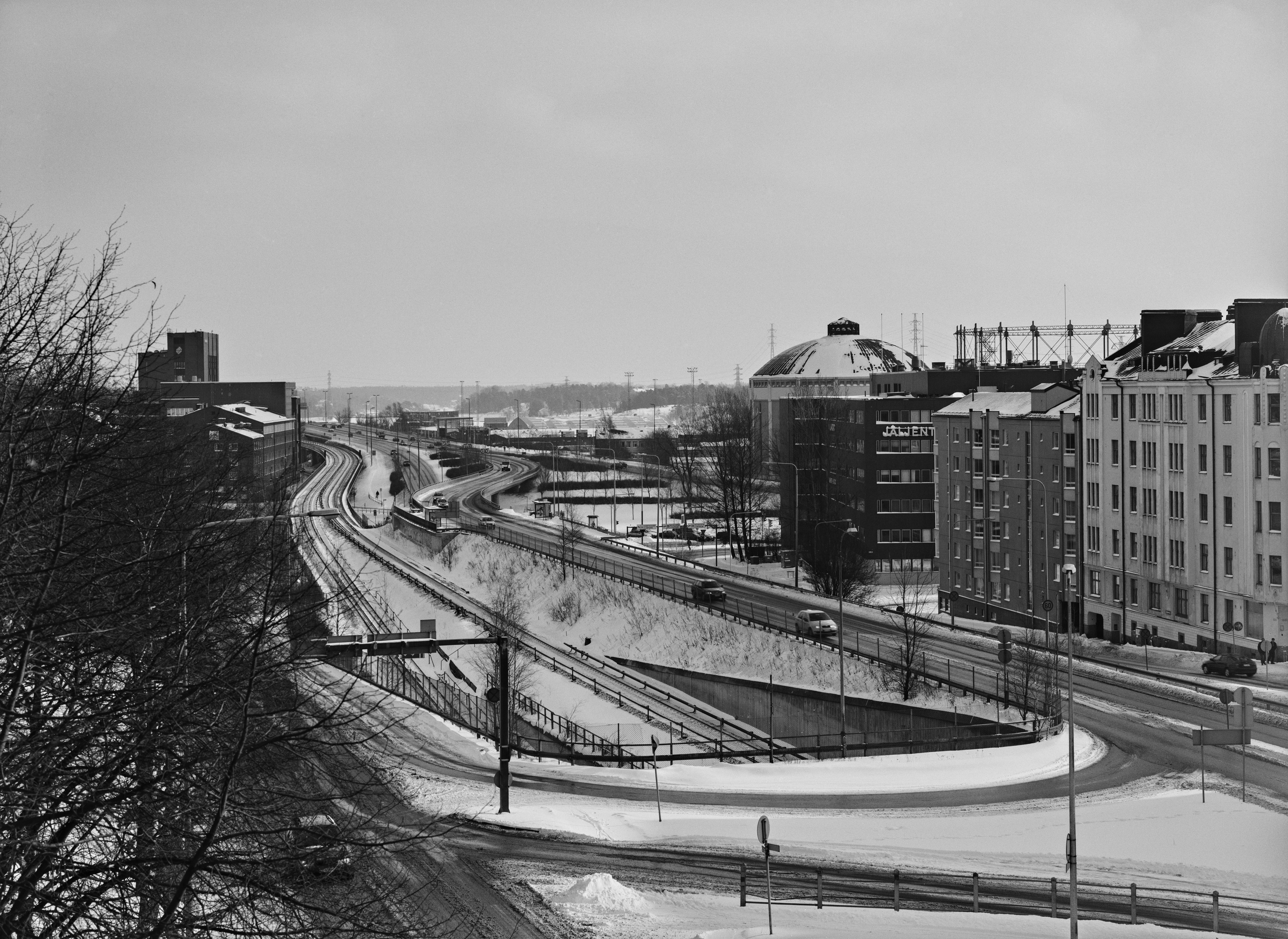 Näkymä Sörnäisistä Sörnäisen ja Vallilan yhdistävältä sillalta Kulosaaren sillan suuntaan. Oikealla Pääskylänkatu 9, 11 ja 13 sekä niiden takana Suvisaaren kaasukello. Pääskylänkadun vasemmalla puolella metroliikenteen ulostulo- ja sisäänmenoväylät Sörnäisten asemalle. Metrolinjasta vasemmalle näkyy Lautatarhankadun toimistorakennuksia. Maahan on satanut kevyesti uutta lunta.