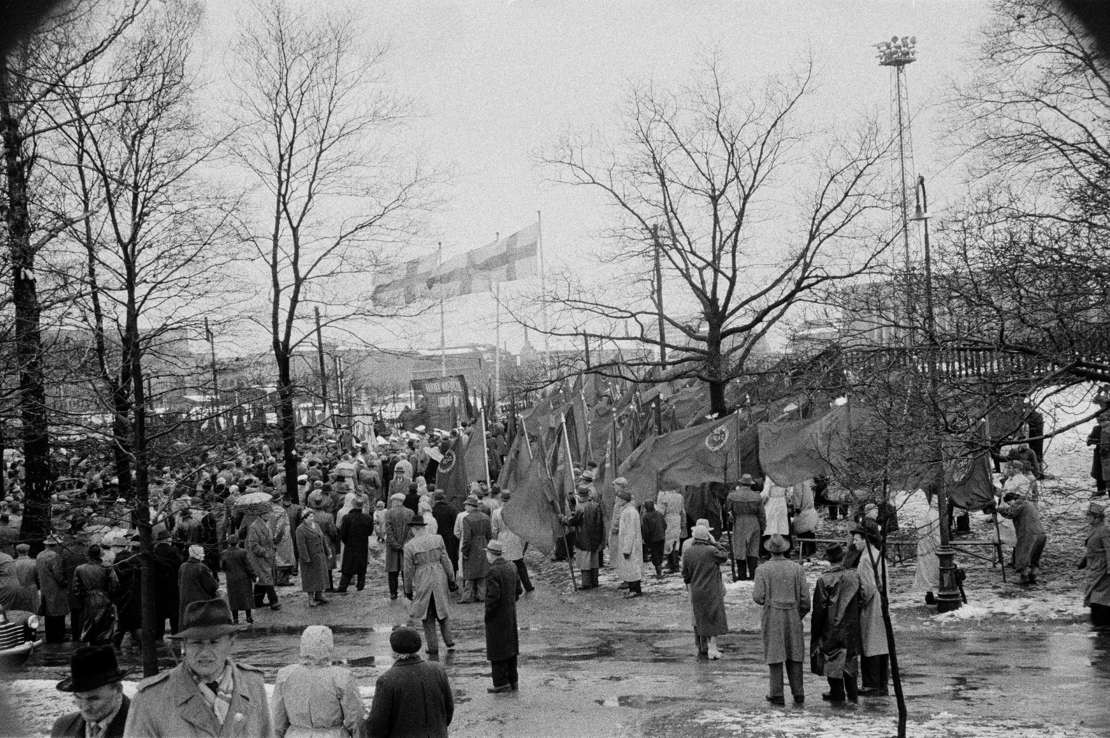 Työväen vappujuhla lumi- ja räntäsateessa Kaisaniemen kentällä 1957. Keskellä Suomen Kommunistisen Puolueen (SKP) lippujen kantajia.