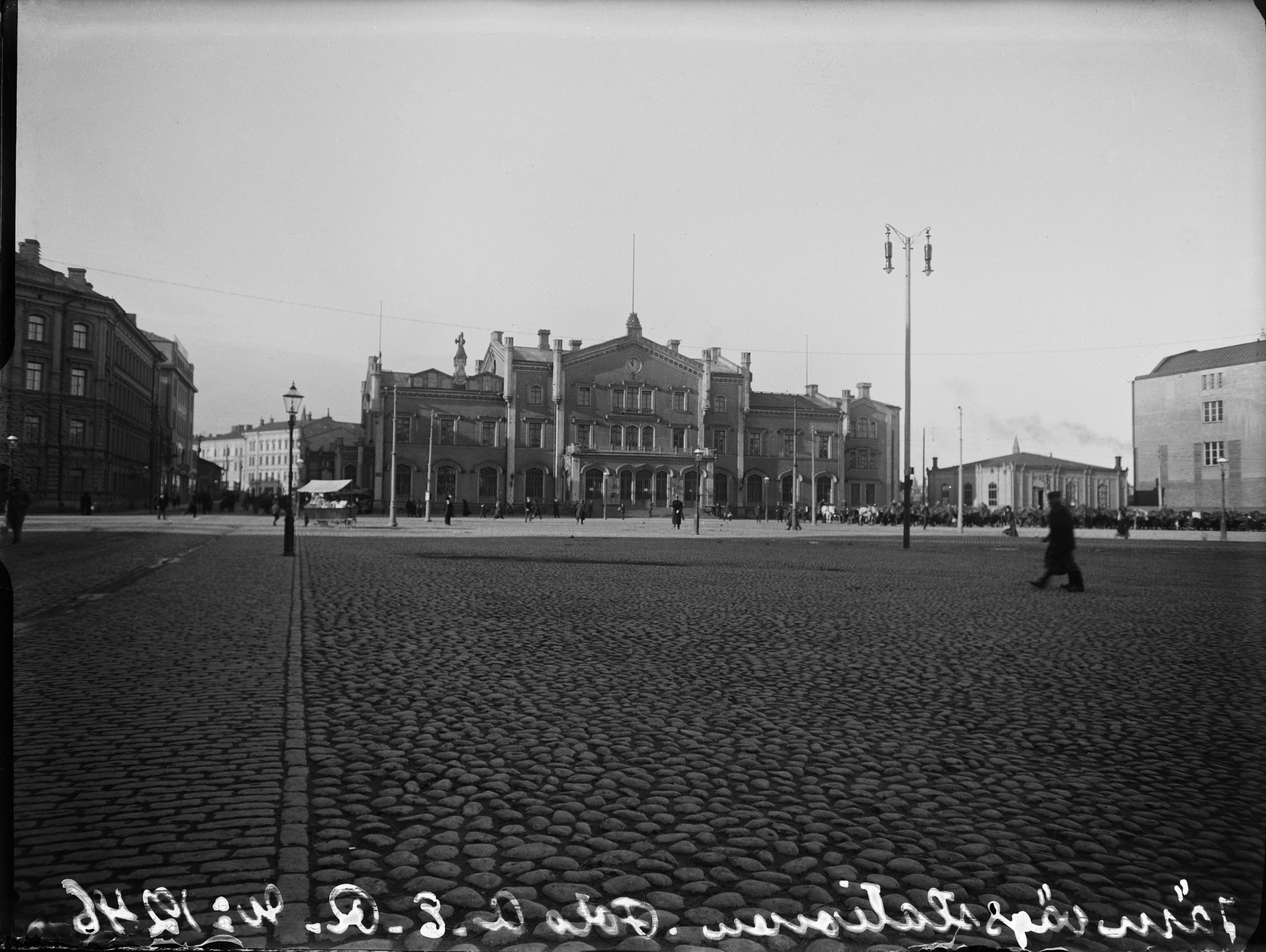 Helsingin vanha rautatieasema, oikealla vuokra-ajureita sekä uuden rautatieaseman hallintorakennuksen pääty (valmistunut 1909). Vasemmalla Skohan talo (Kaivokatu 6 - Keskuskatu 8).