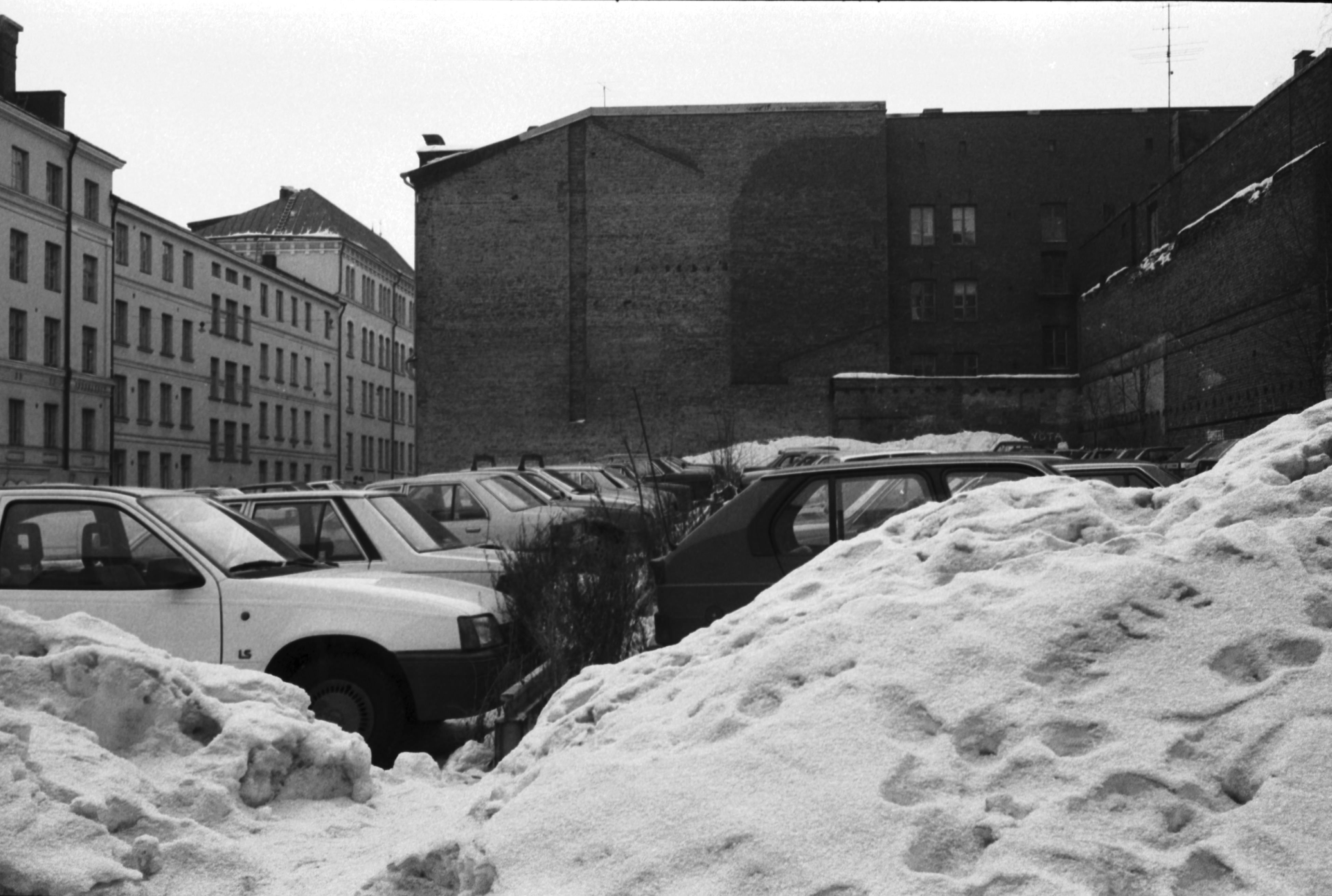 Kirkkokatu 4. Meritullinkatu 8. Pysäköityjä autoja lumikasojen keskellä rakentamattomalla tontilla Kirkkokadun ja Meritullinkadun kulmassa. Taustalla Meritullinkatu 6:n pääty, vasemmalla Meritullinkatu 1.