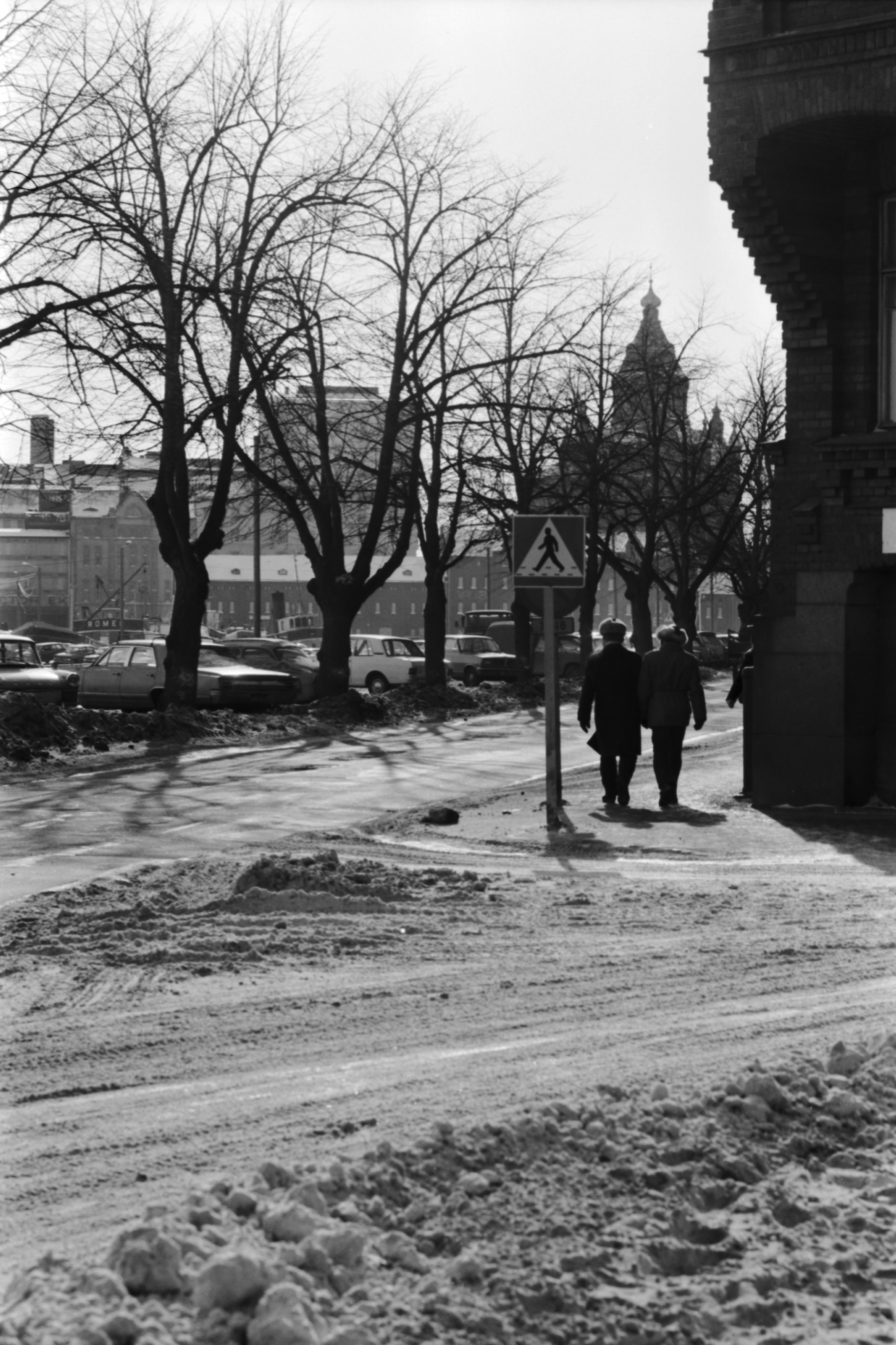 Kaksi miestä kävelemässä Pohjoisrannan ja Maneesikadun kulmassa. Oikealla Kenraalien talon kulma, taustalla Uspenskin katedraali. Talvinen näkymä Liisanpuistikon nurkalta Katajanokan suuntaan.