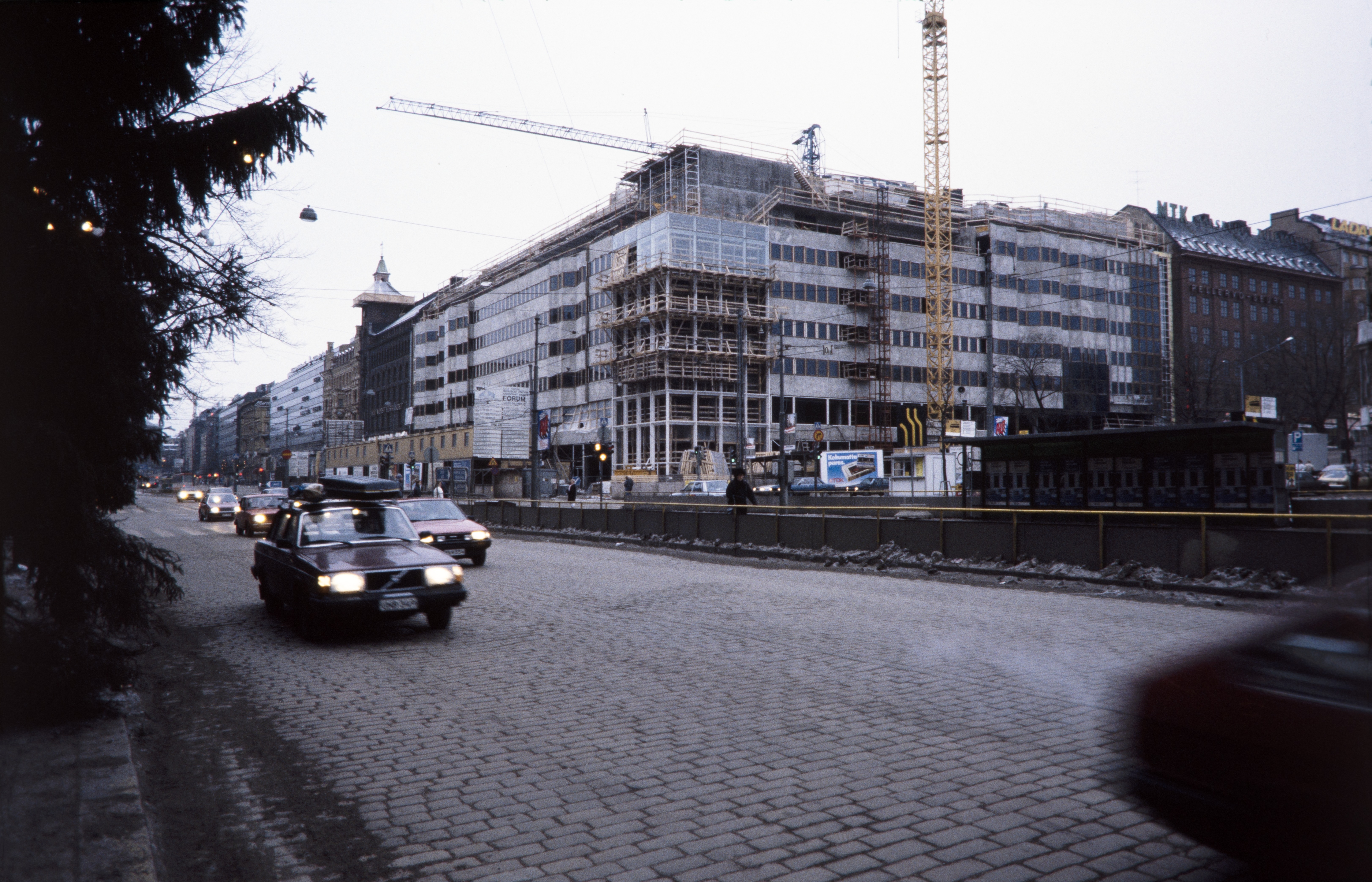 Forumin kauppakeskus rakenteilla harjakorkeudessaan.. Mannerheimintie 20 - Simonkatu 2. Rakennustyömaalla nostokurkia. Mannerheimintiellä henkilöautoja, keskellä raitiovaunupysäkki.