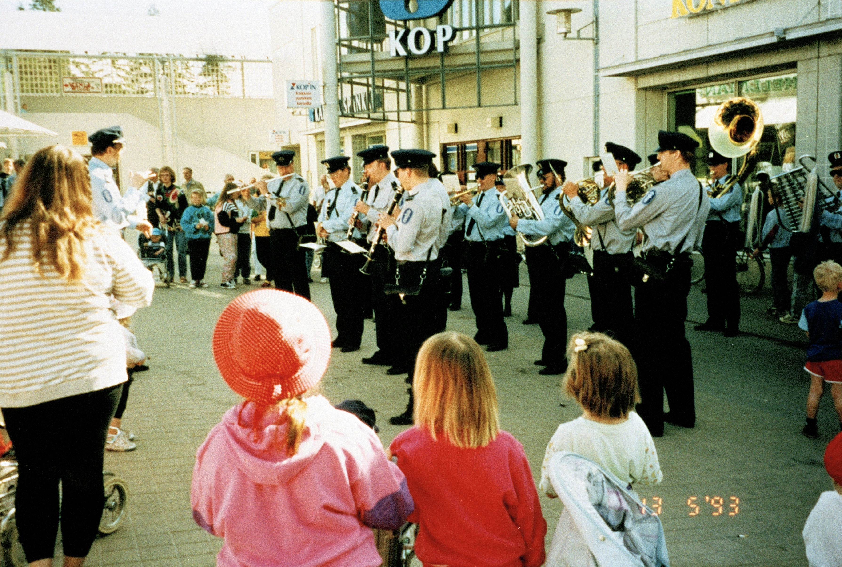 Poliisien soittokunta viihdyttää ihmisiä Kukanpäivän juhlassa Kontulan ostoskeskuksessa. Taustalla KOP:n konttori.