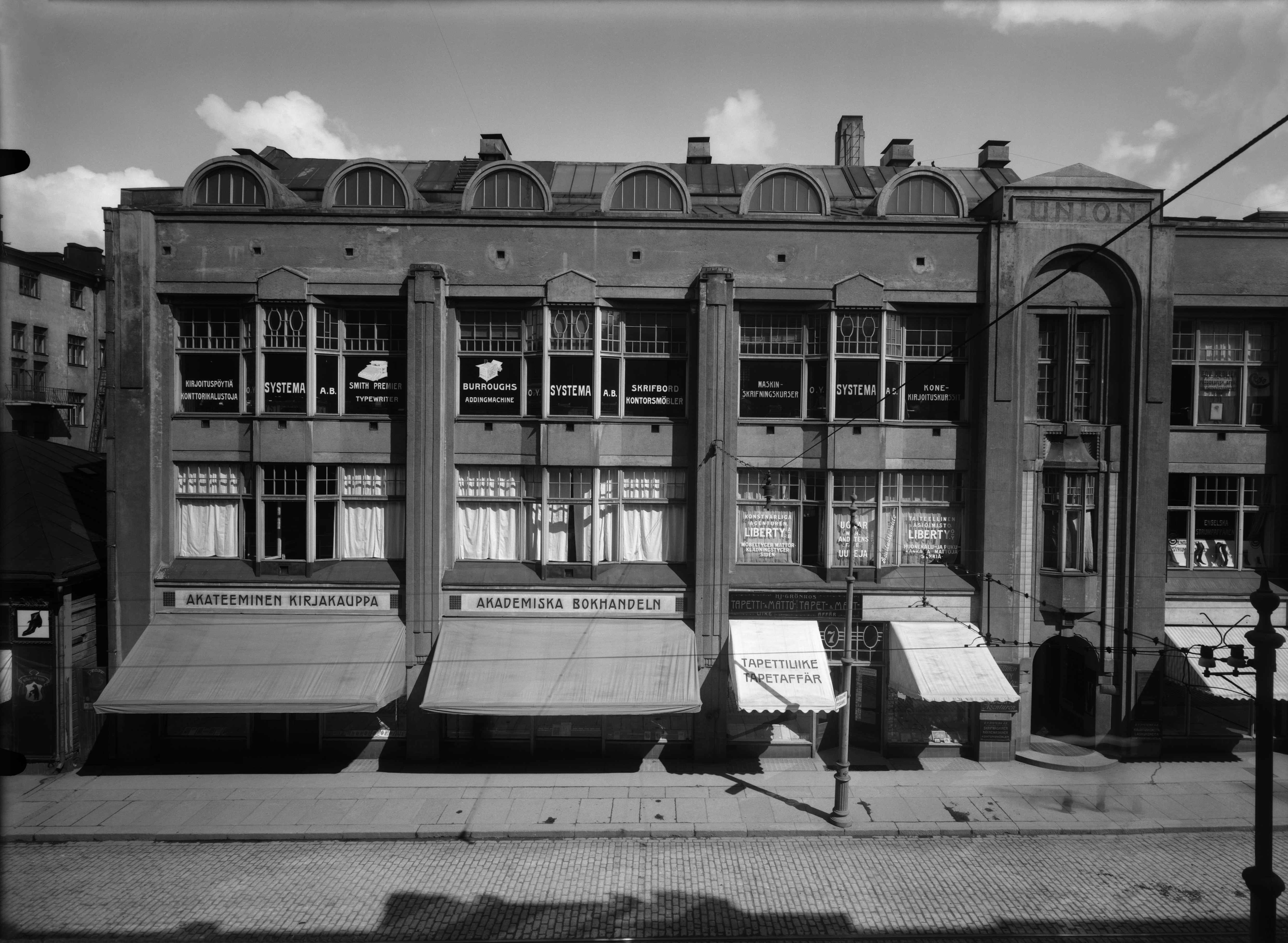 Aleksanterinkatu 7 b:ssä sijaitsi 1910-luvun loppupuolella mm. Akateeminen kirjakauppa, kirjoituspöytiä ja konttoritarvikkeita myyvä Systema, tapettiliike, sekä taiteellinen asiaimisto Liberty.