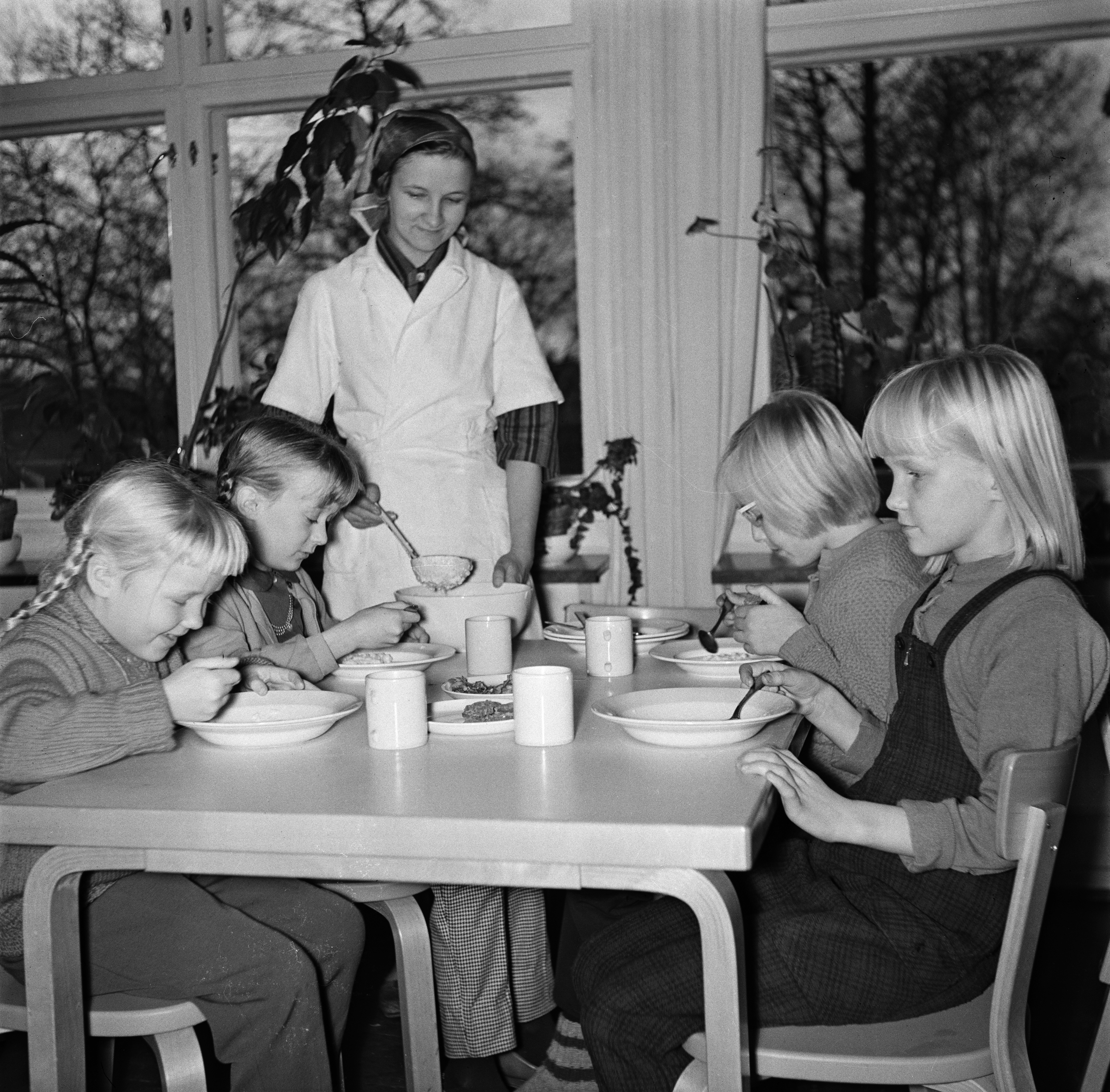 Koululaiset ruokailemassa Vallisaaren kansakoulussa. Ruokaa jakamassa koulurakennuksen talonmies Nieminen. Valokuva on otettu syksyllä.
