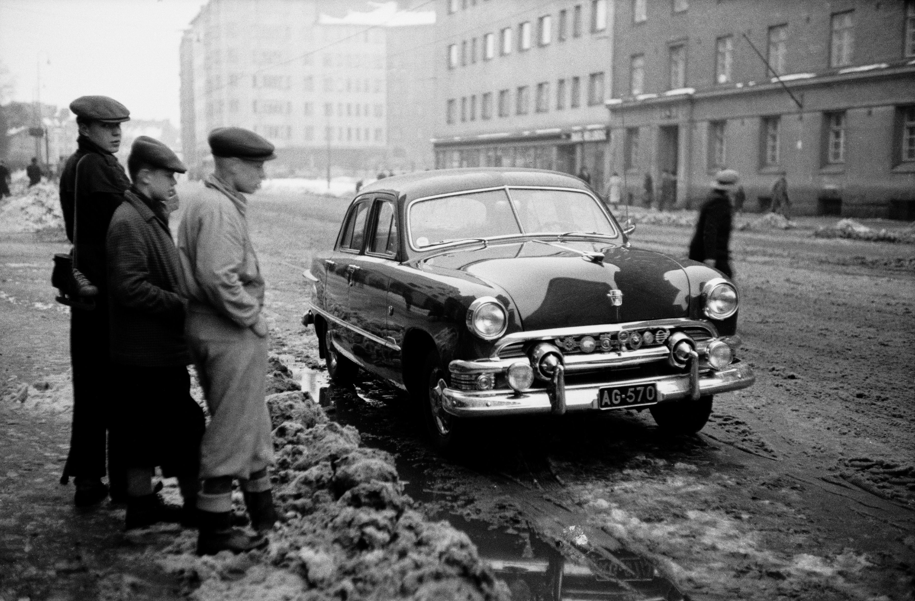 Kolme poikaa katselemassa Helsinginkatu 9:n eteen parkkeerattua autoa (neliovinen Ford sedan, vm. 1951). Taustalla Harjutori sekä Helsinginkatu 6, 10.