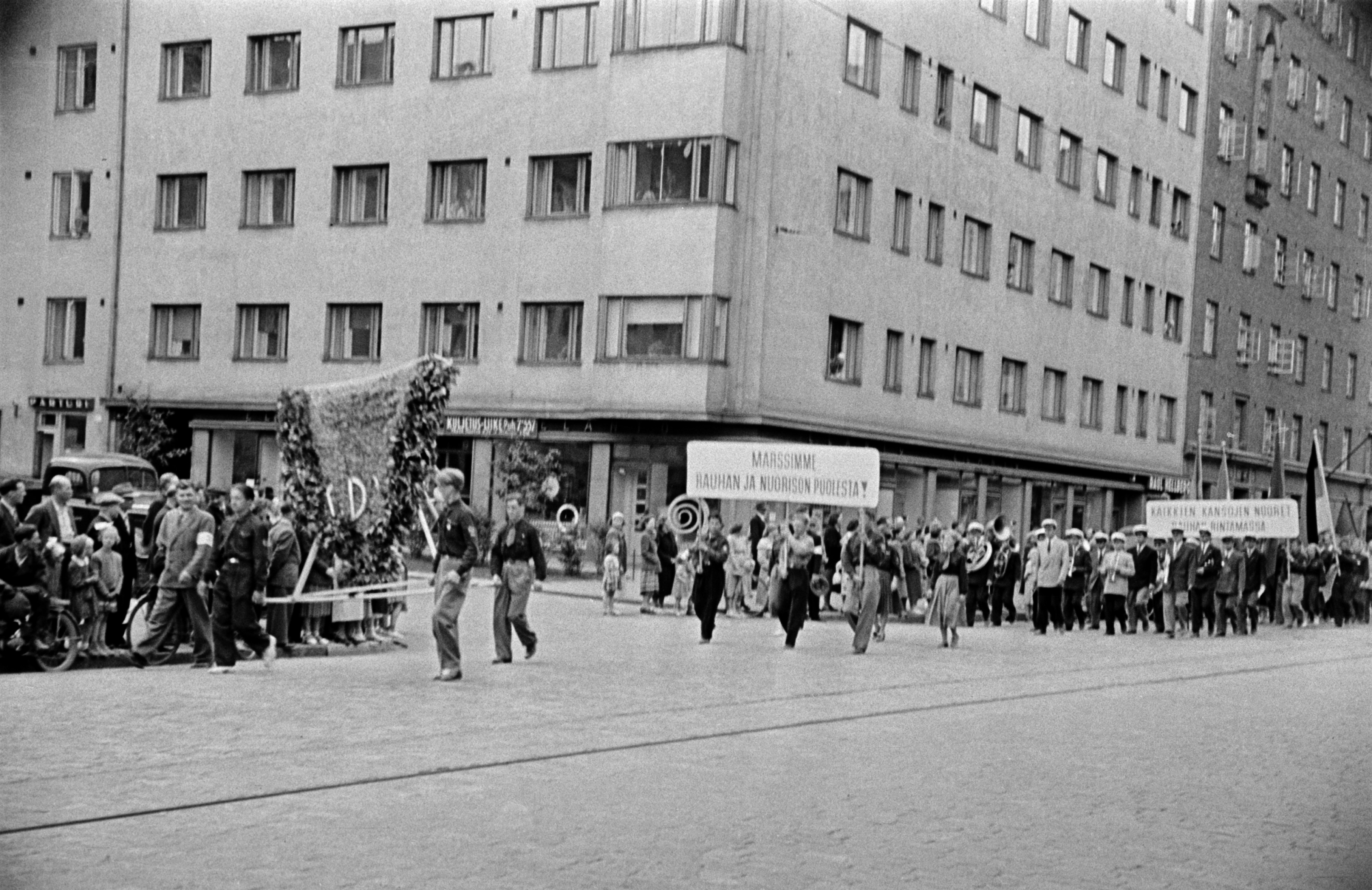 Rauhanmarssi ja yleisöä Helsinginkadulla Harjutorin kohdalla, Suomen Demokratian Pioneerien Liiiton (SDPL) jäseniä, joilla seppele sekä kyltti "Marssimme rauhan ja nuorison puolesta".