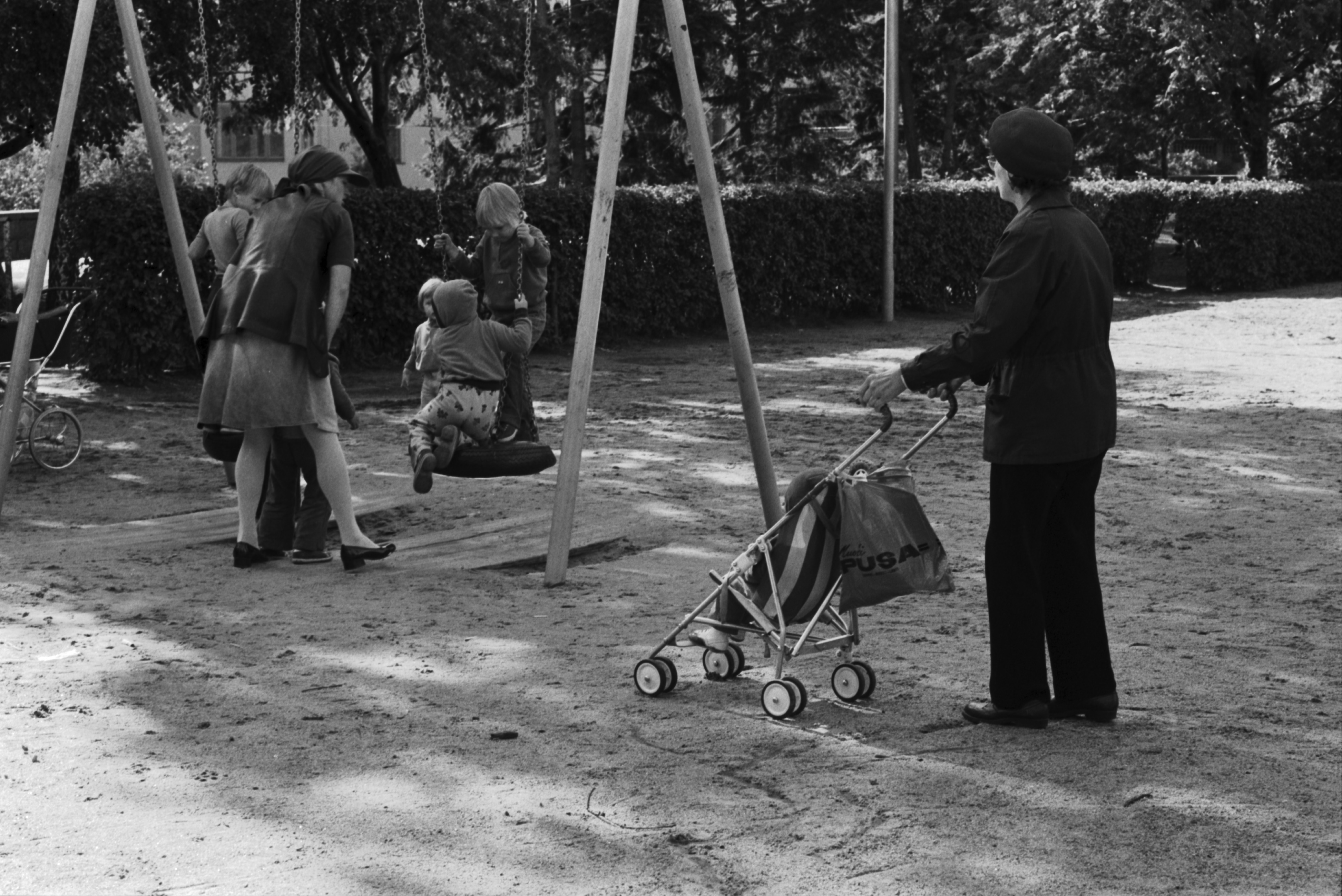 Tehtaanpuisto. Lapsia äiteineen ja hoitajineen keinumassa Tehtaanpuiston leikkipaikalla.
