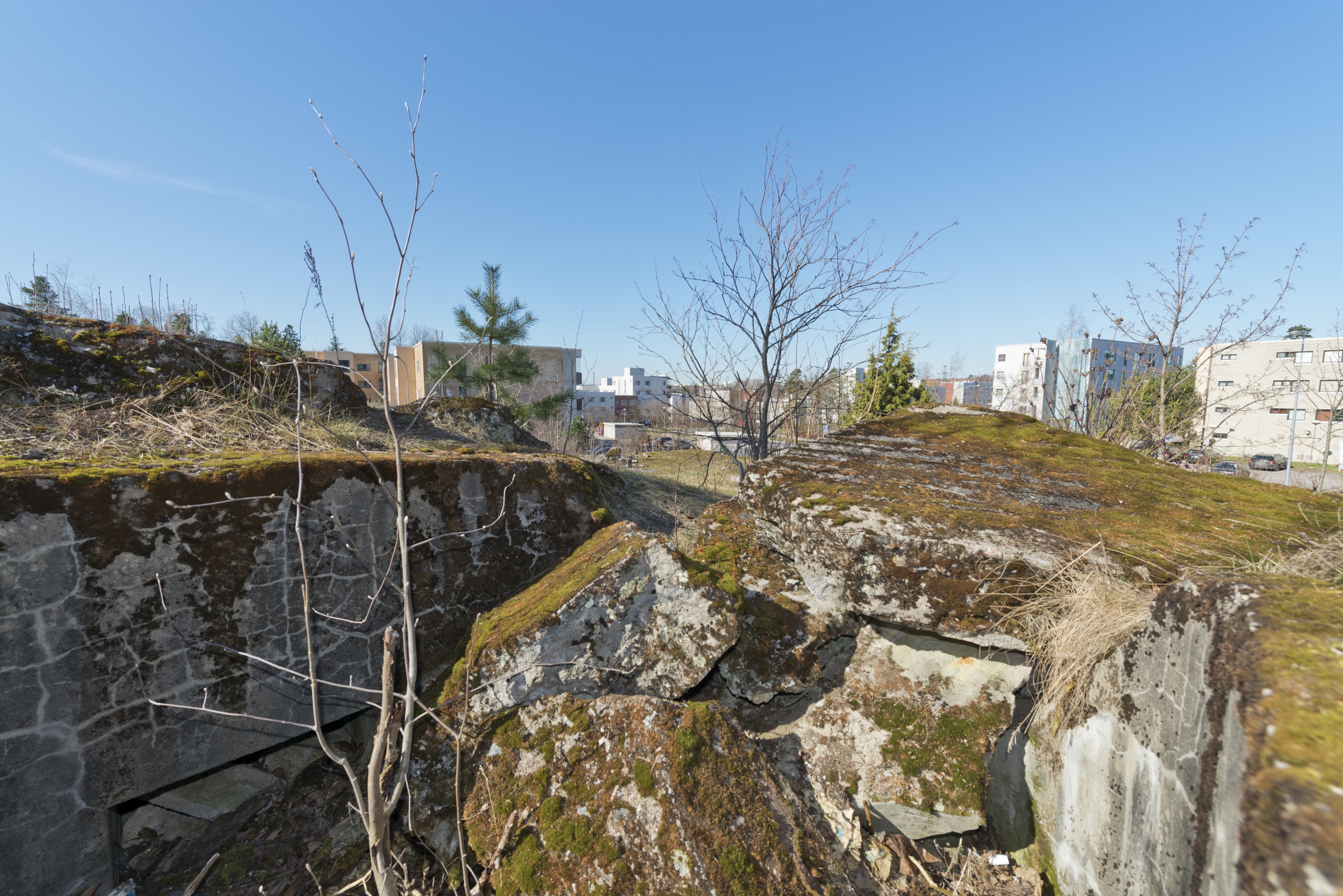Länsimäki. Ensimmäisen maailmansodan aikainen maalinnoitus, puolustusasema II:8 Länsimäessä, Vantaalla. Kuvassa betoninen kaarevaa mallia oleva konekivääriasema aseman länsiosassa. Aseman katto on räjäytetty. Betoninpalat täyttävät aseman ja ampumasektorin. Seinässä vasemmalla erottuu toisen komeron yläreuna. Taustalla näkyy tie ja asuinrakennuksia. Kuvaussuuntana länsi-lounas.