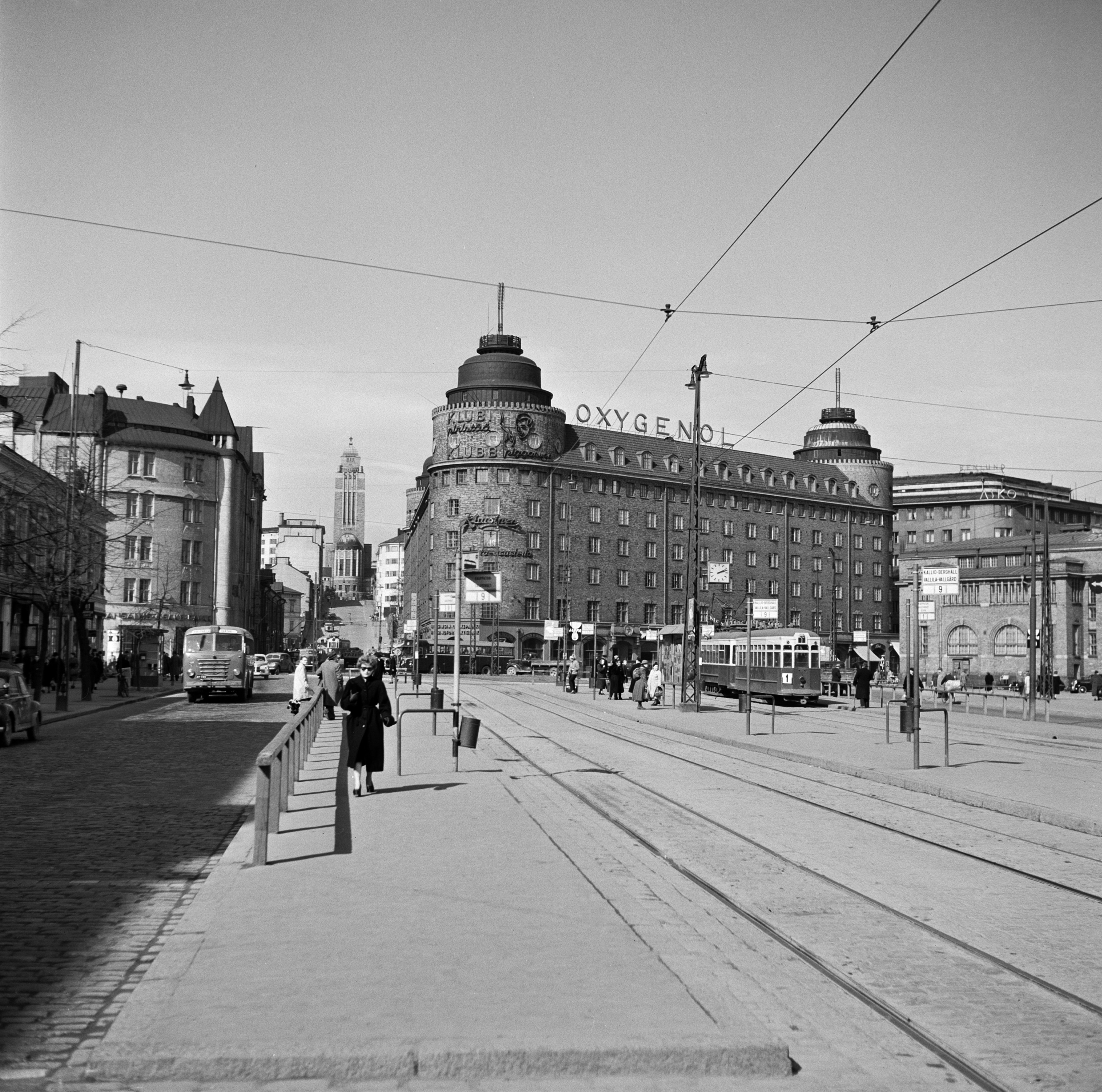 Siltasaarenkadun raitiovaunulaiturit ja raitiovaunuja. Taustalla Arenan talo, Siltasaarenkatu 11 - Hämeentie 2,  ja Hakaniemen kauppahalli.